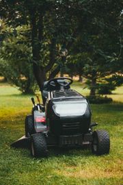 A black lawn mower is parked in the grass next to a tree.