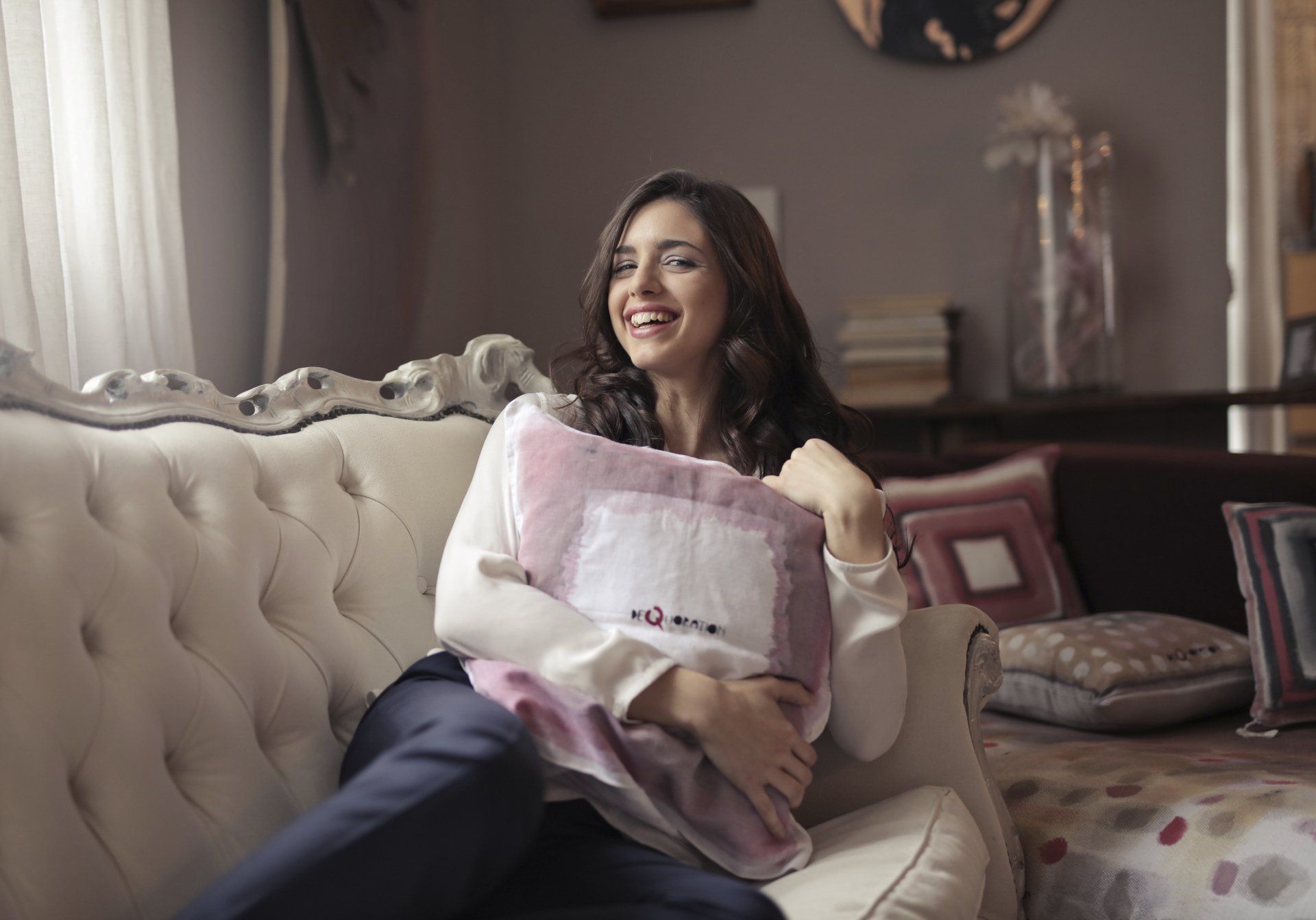 A woman is sitting on a couch holding two pillows in her clean home.