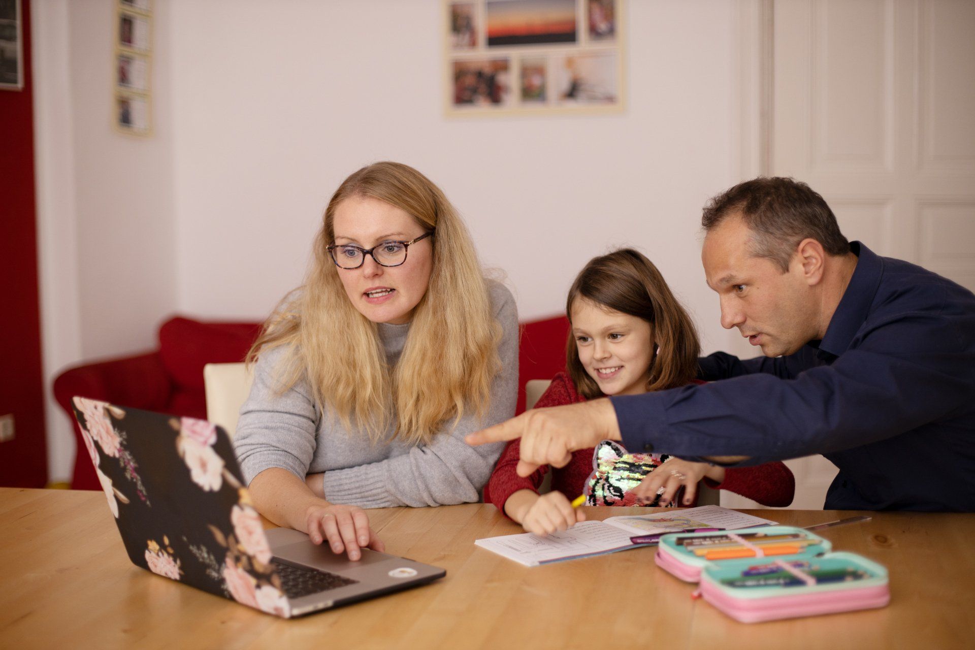a family is sitting at a table looking at a laptop computer .