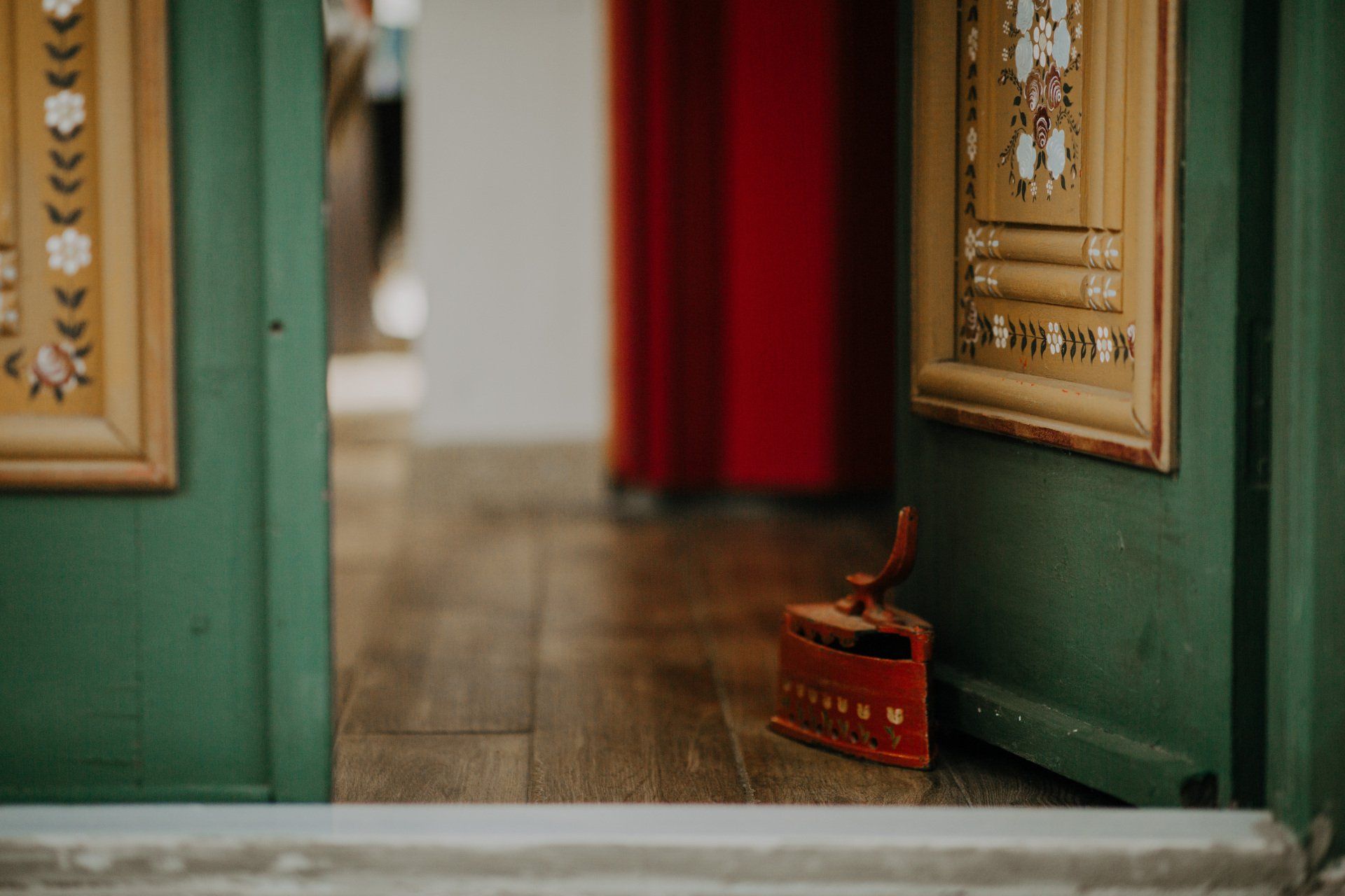 A red iron is sitting on the floor next to a green door.