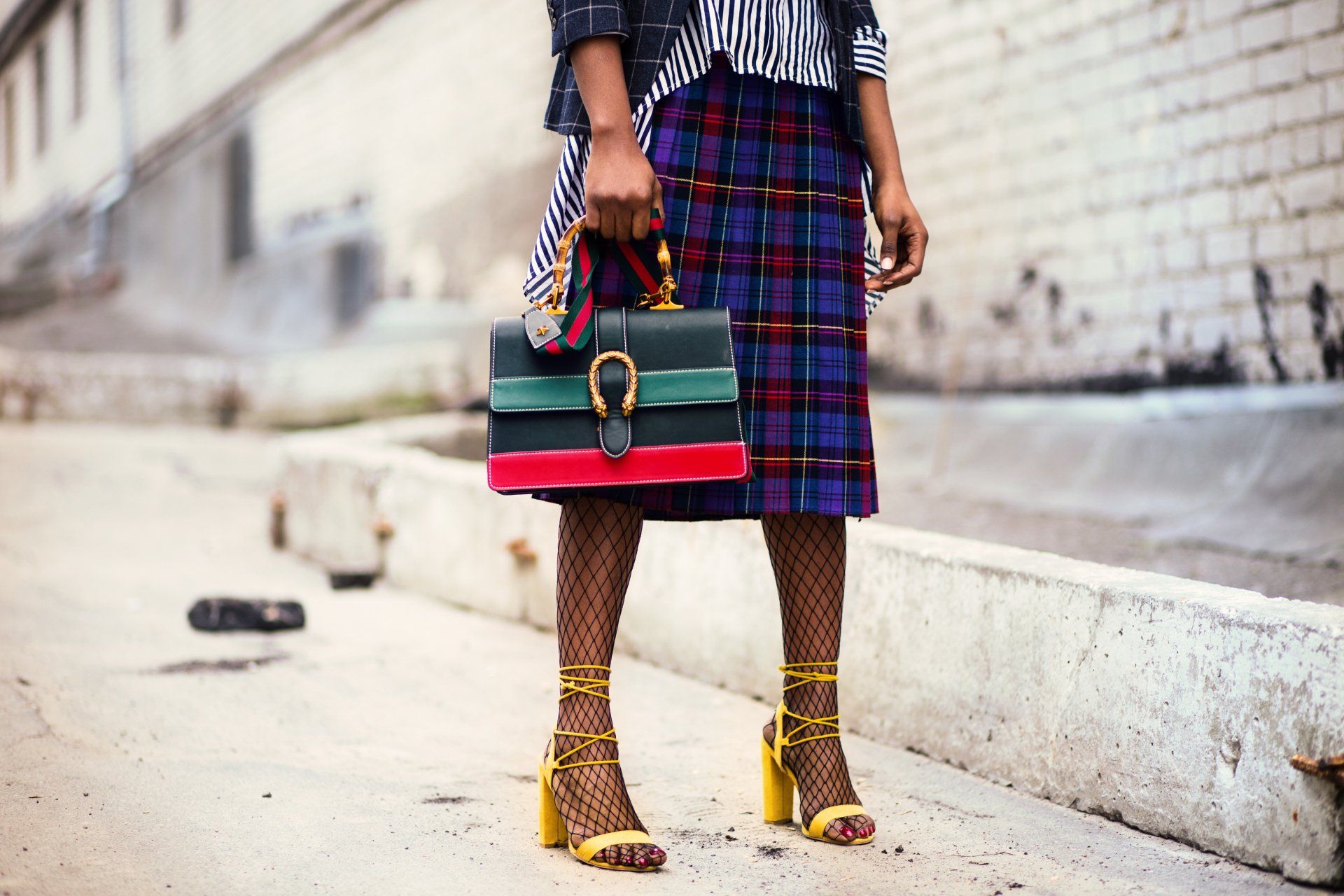 a woman in a plaid skirt is holding a colorful purse