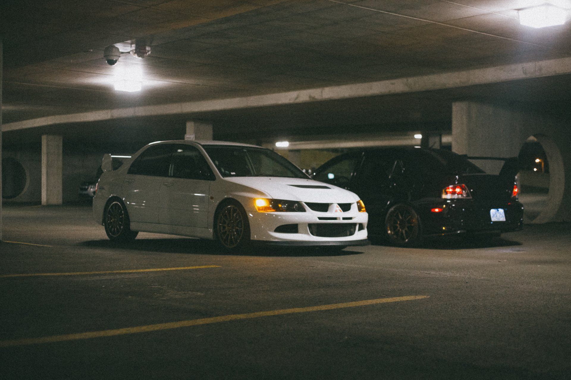 Two cars are parked in a parking garage at night.