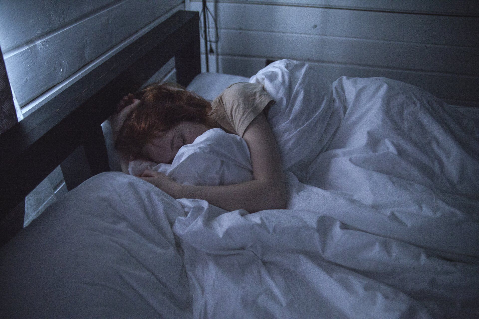 una donna dorme in un letto con lenzuola bianche.