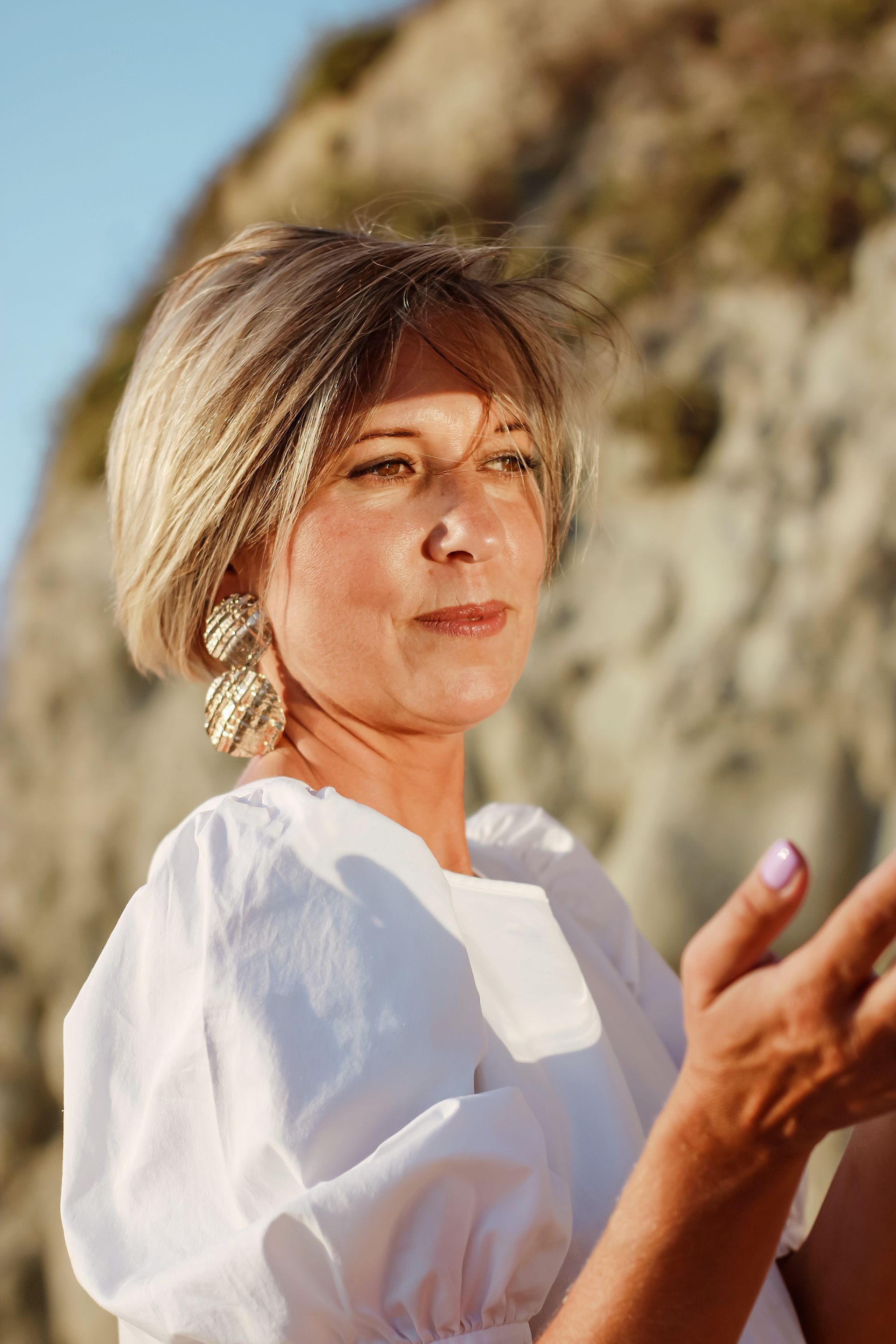 A woman in a white dress and earrings is standing on a beach.