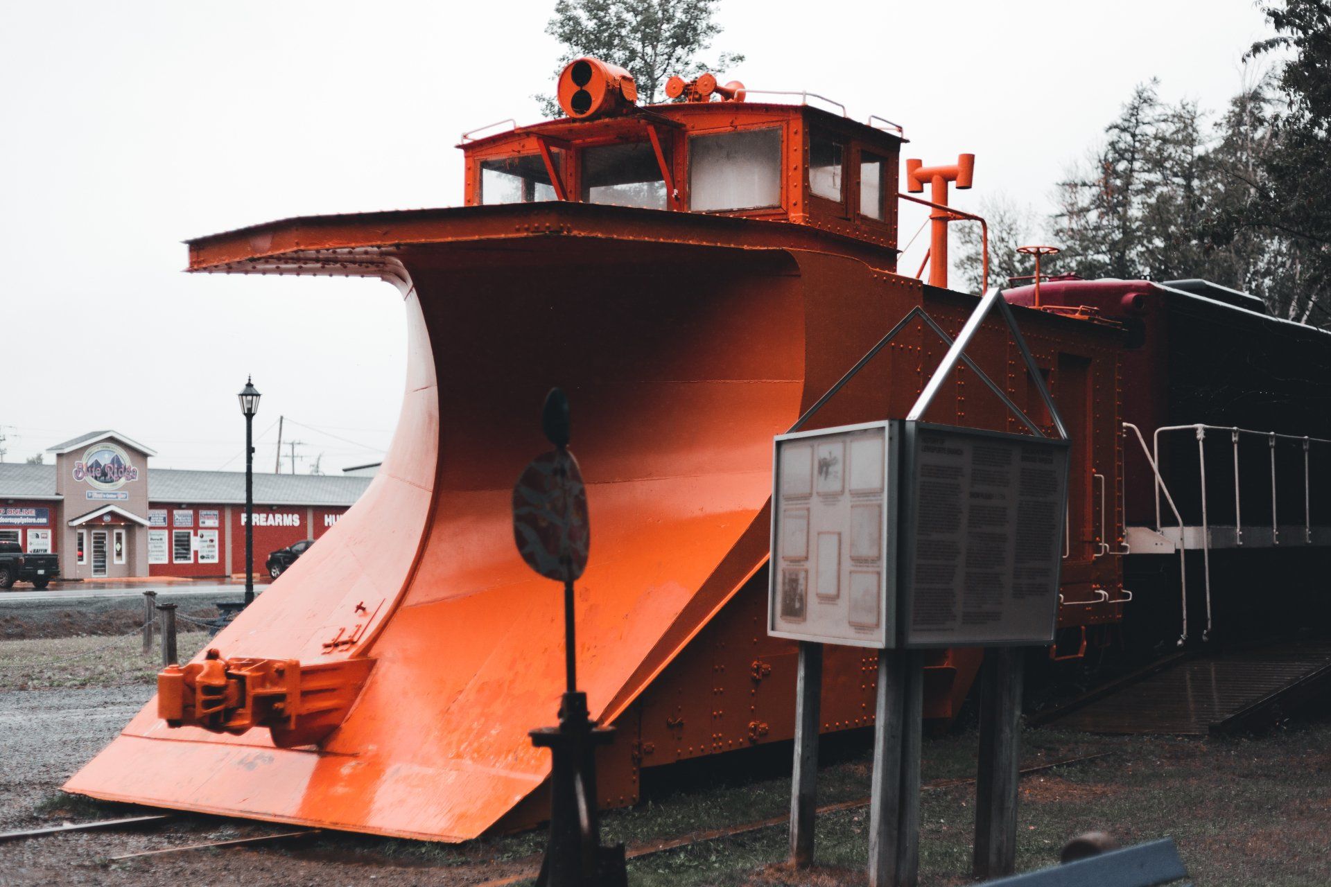 A large orange snow plow is parked in front of a building