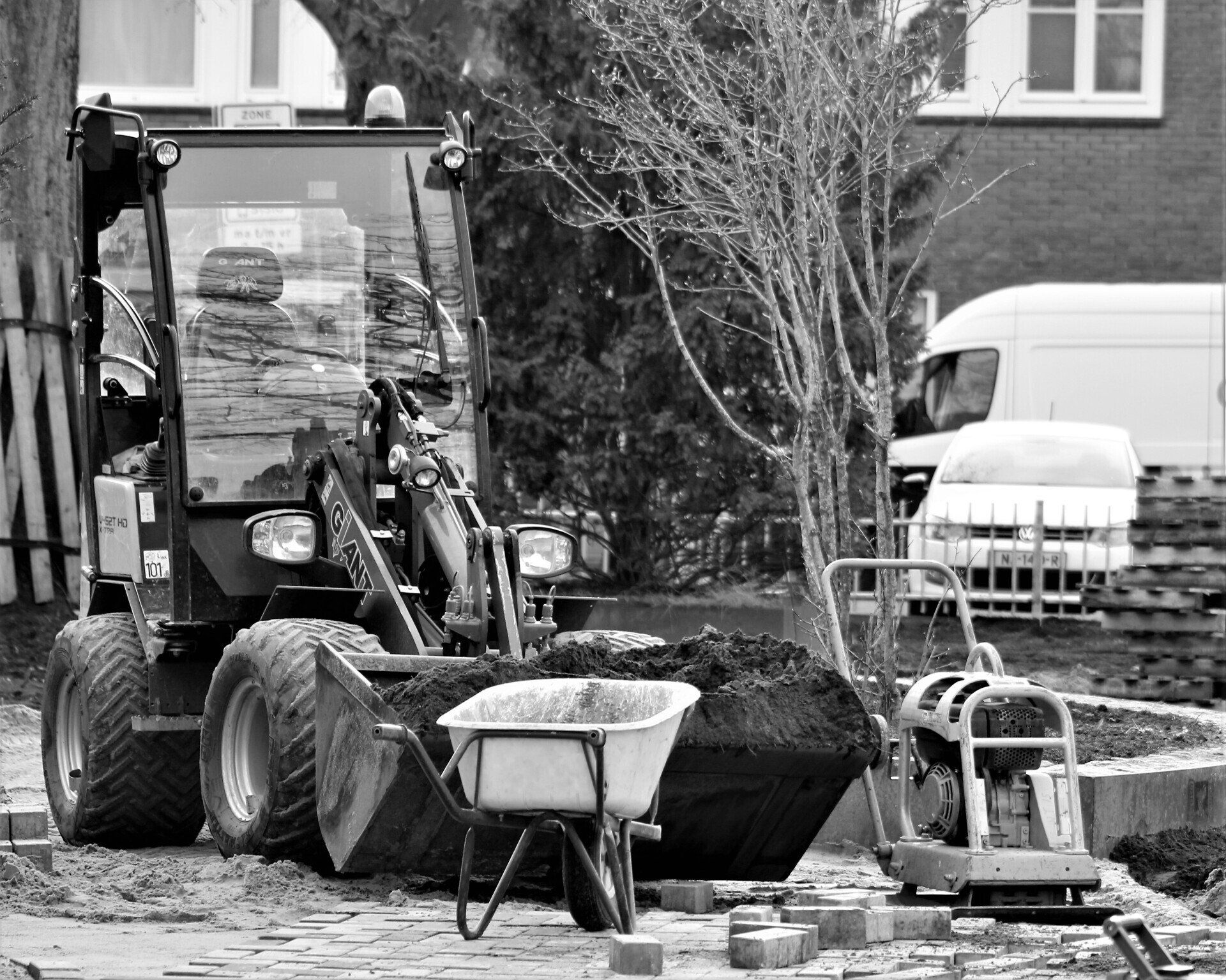 A black and white photo of a construction site with a tractor and a wheelbarrow.