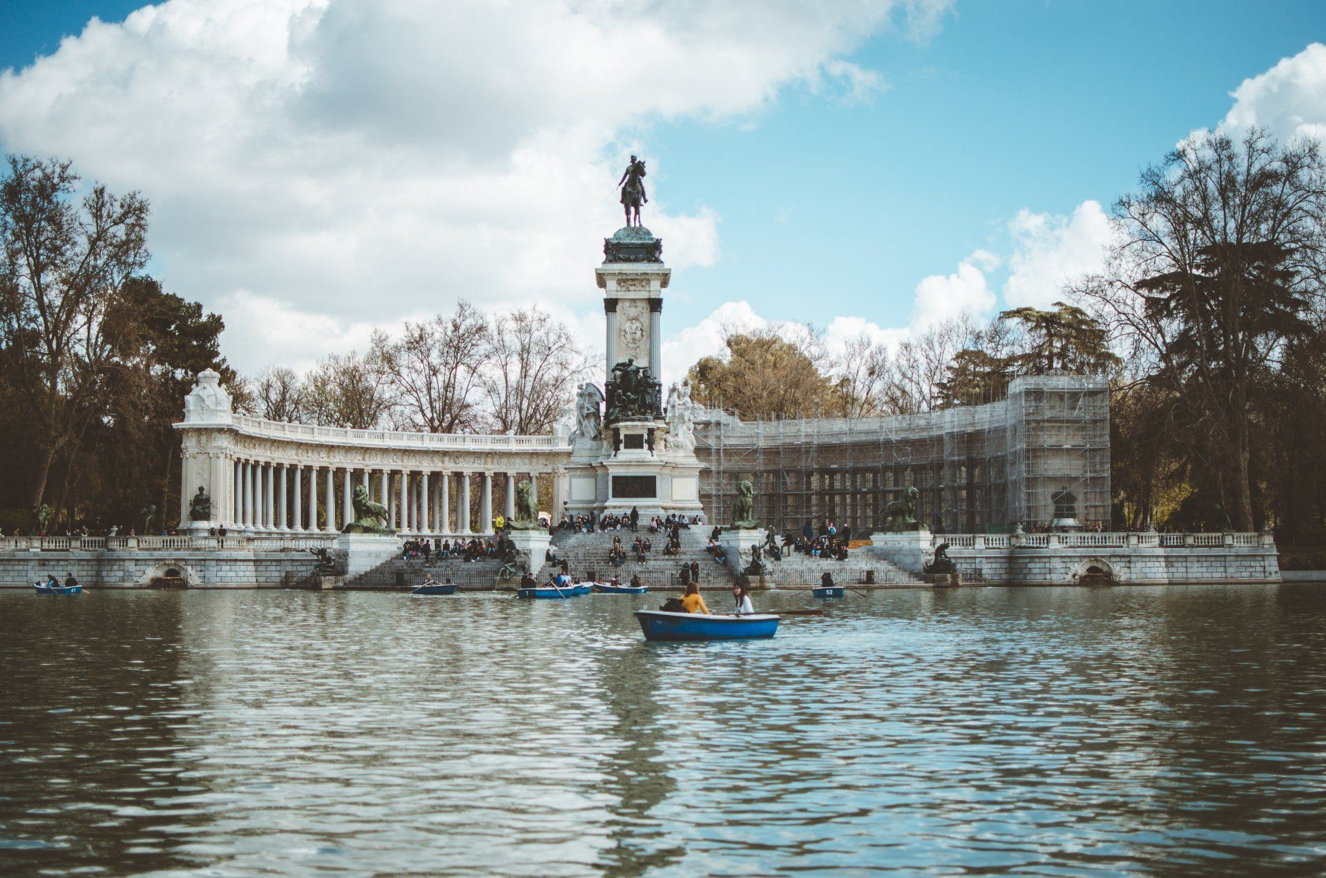 A group of people are rowing boats on a lake in front of a statue.
