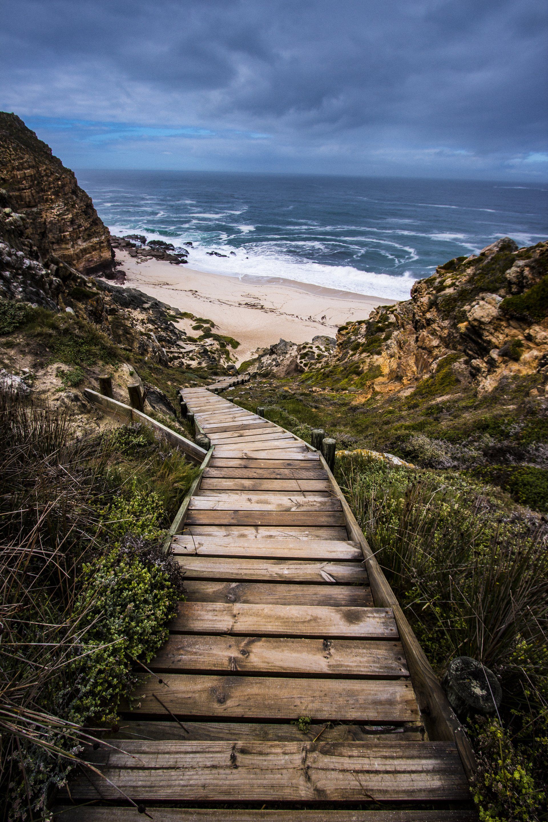 A wooden walkway leading to a beach on a cloudy day.