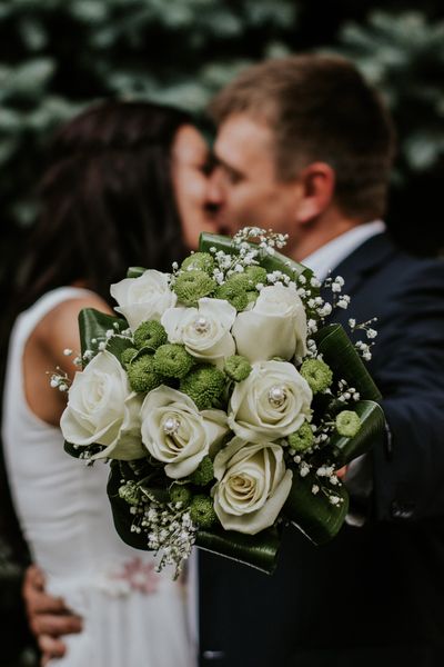 A bride and groom kissing while the bride holds a bouquet of white roses.