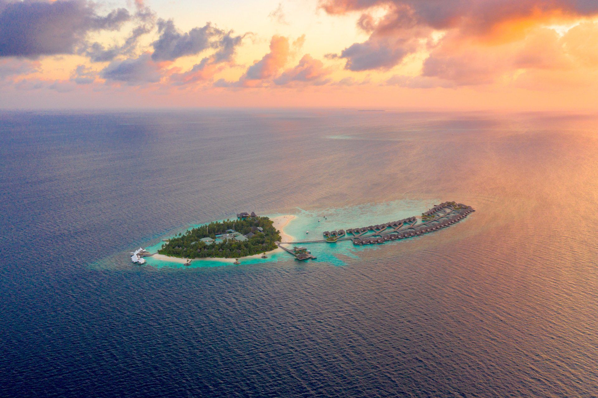An aerial view of a small island in the middle of the ocean at sunset.