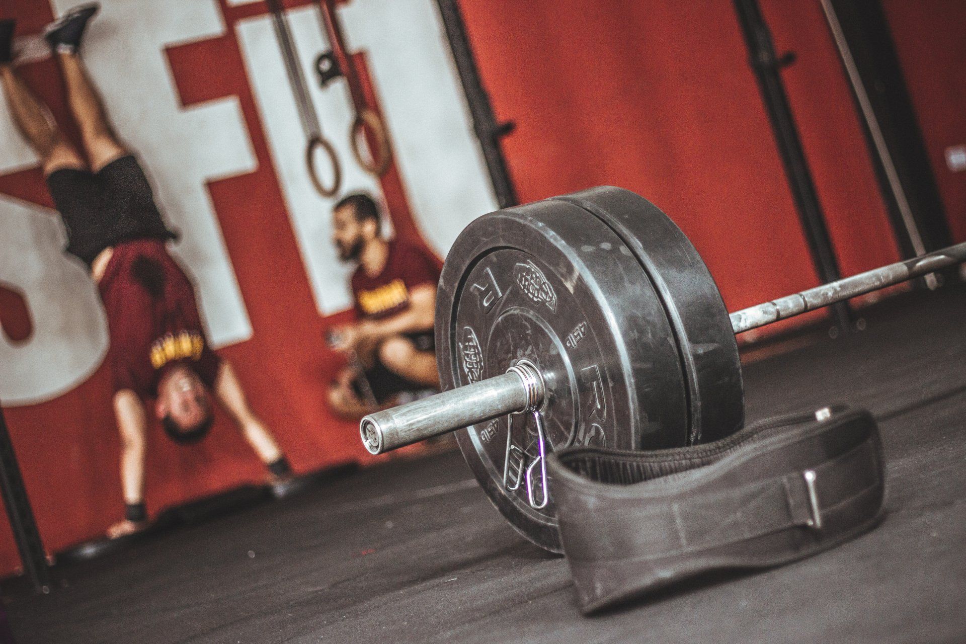 Barbell with weights and weightlifting belt, person doing handstand in CrossFit gym.