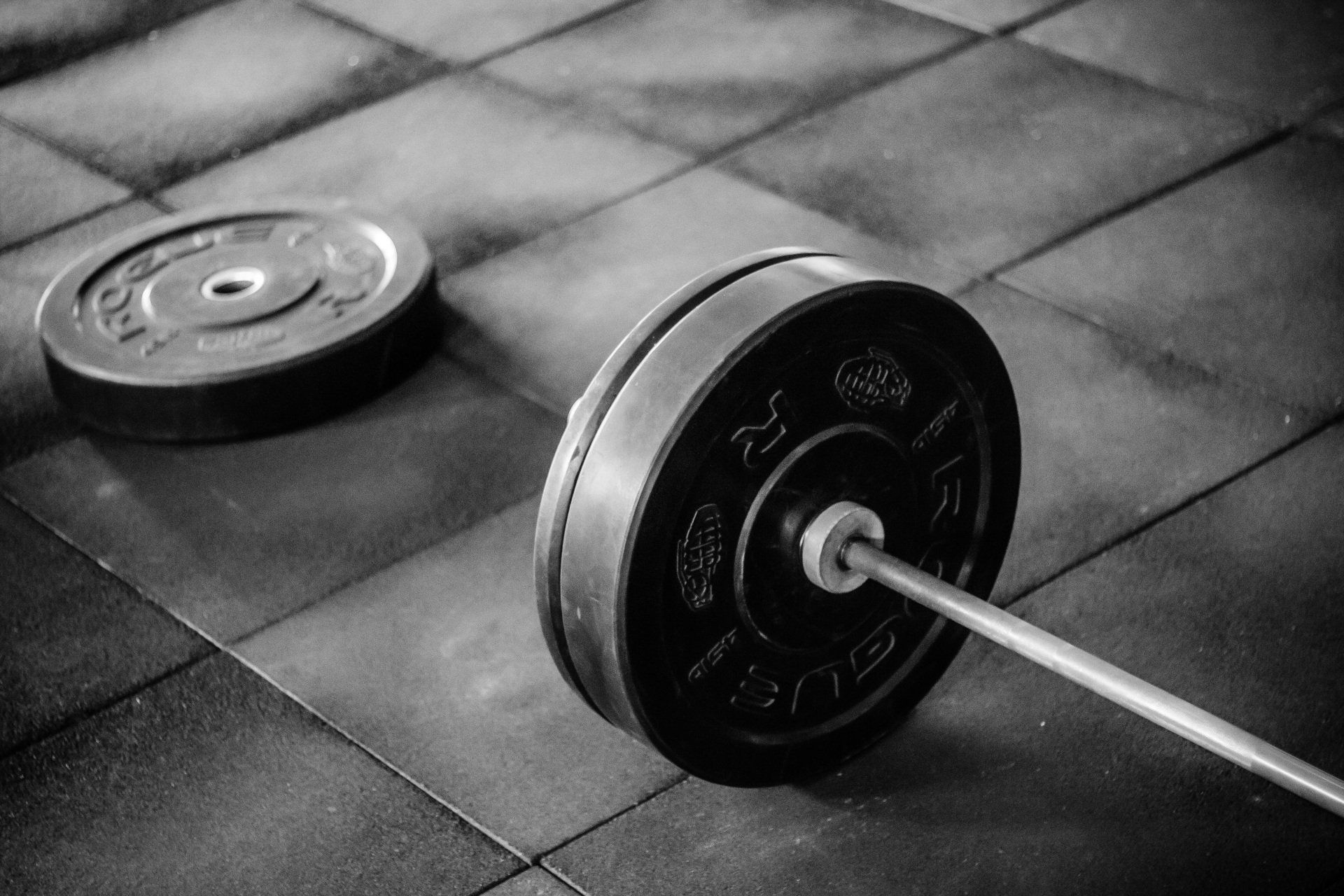 A black and white photo of a barbell on a tiled floor.