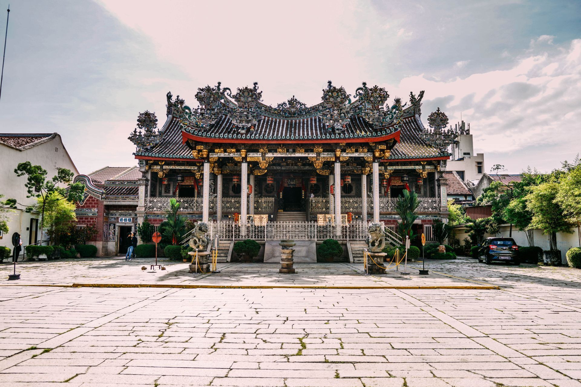 A large chinese building with a red roof is surrounded by trees.
