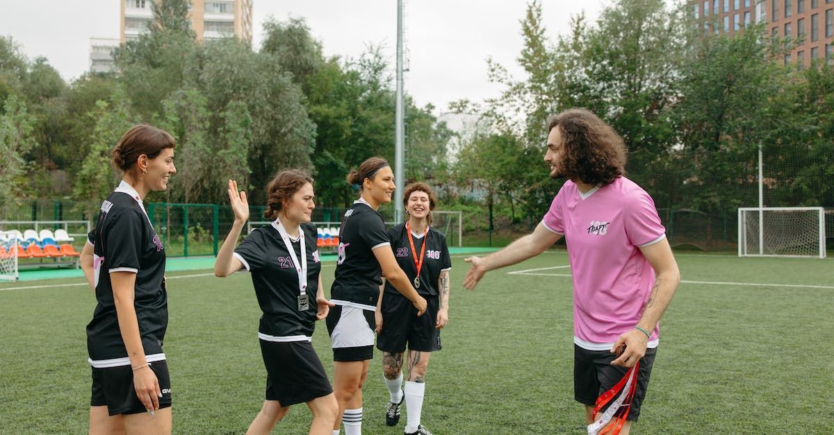 a man in a pink shirt is shaking hands with a group of soccer players on a field .