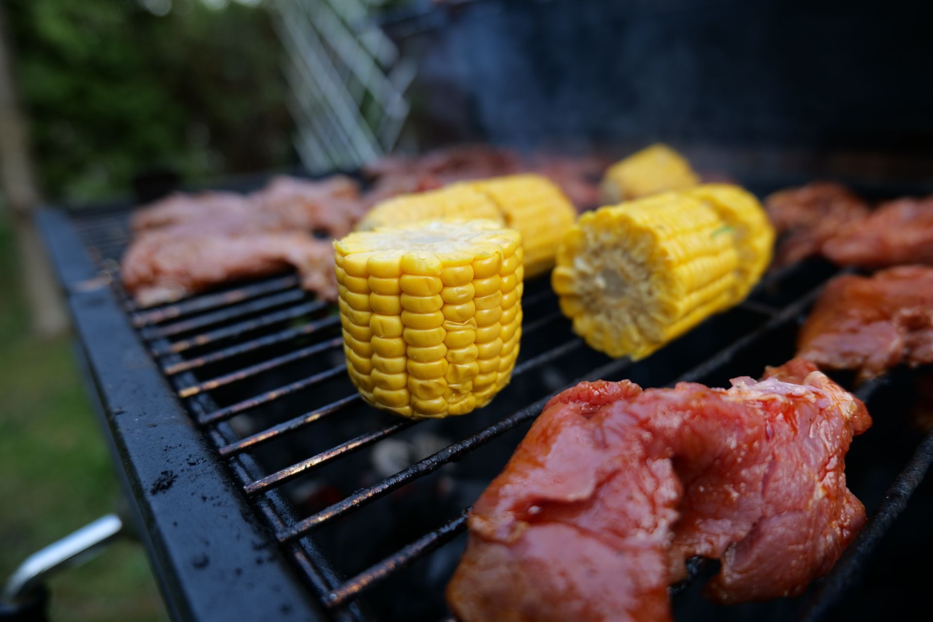 Corn on the cob and meat are cooking on a grill.