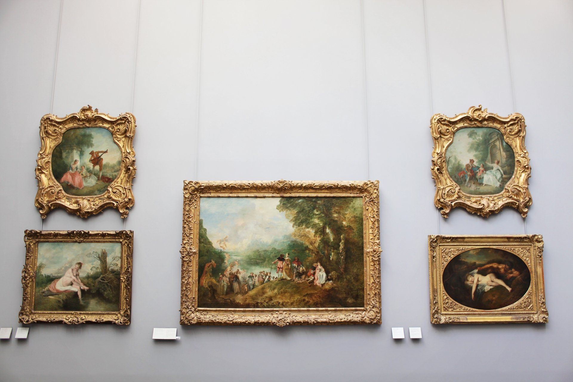 Several paintings are hanging on a wall in a museum
