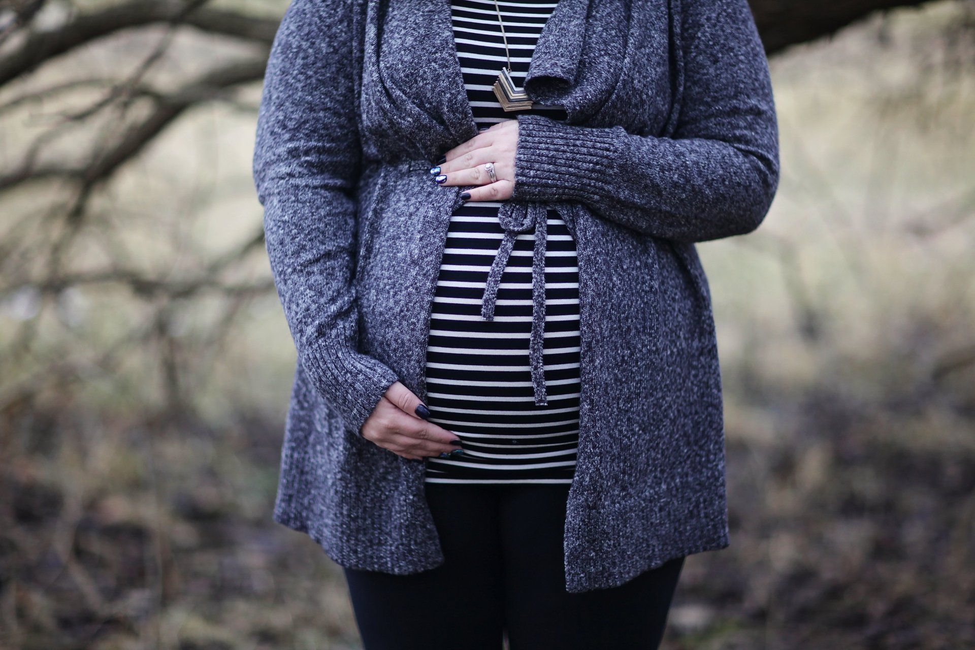 A pregnant woman in a striped shirt and cardigan is holding her belly.