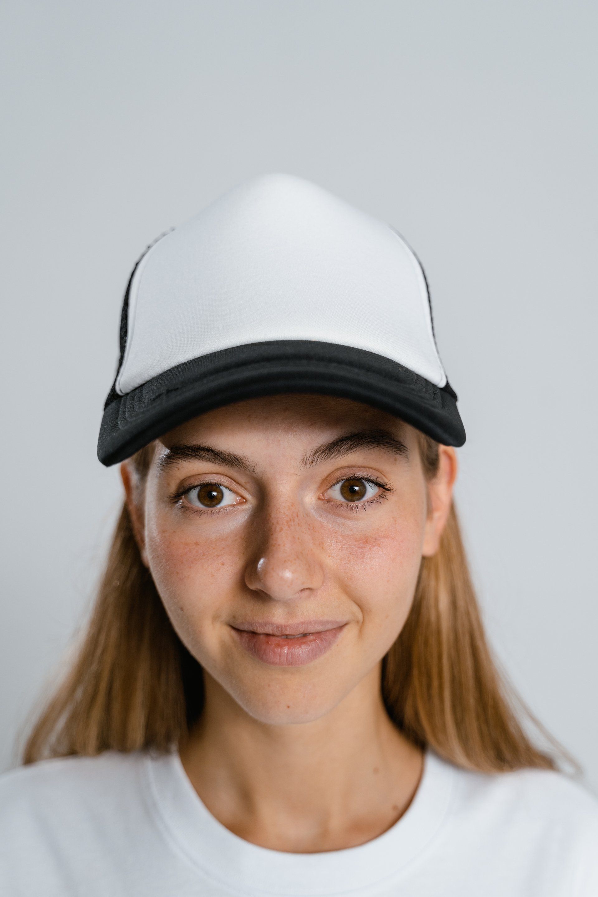 A young woman wearing a white trucker hat and a white t-shirt.