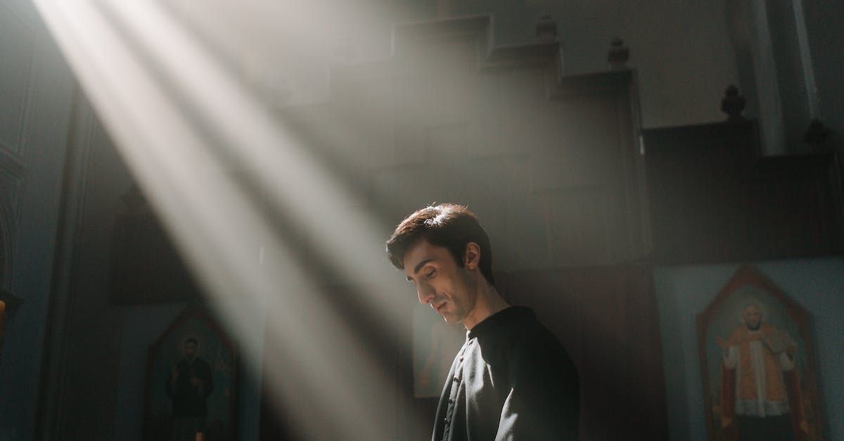 A man is standing in a dark room with the sun shining through the window.