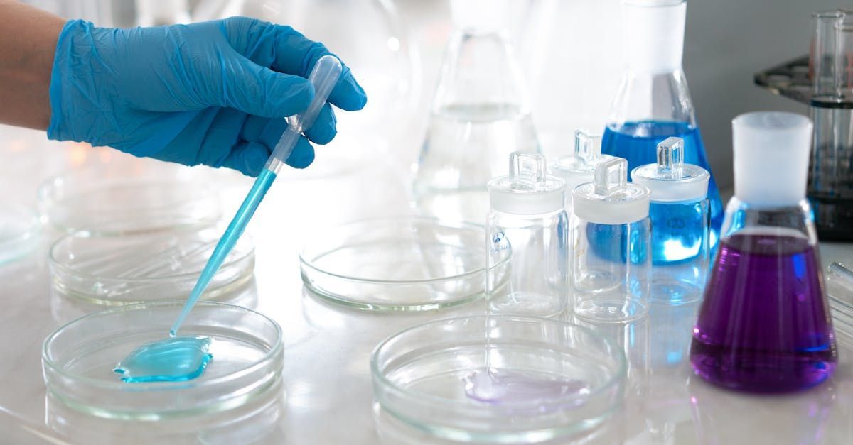 A person is pouring a blue liquid into a petri dish.