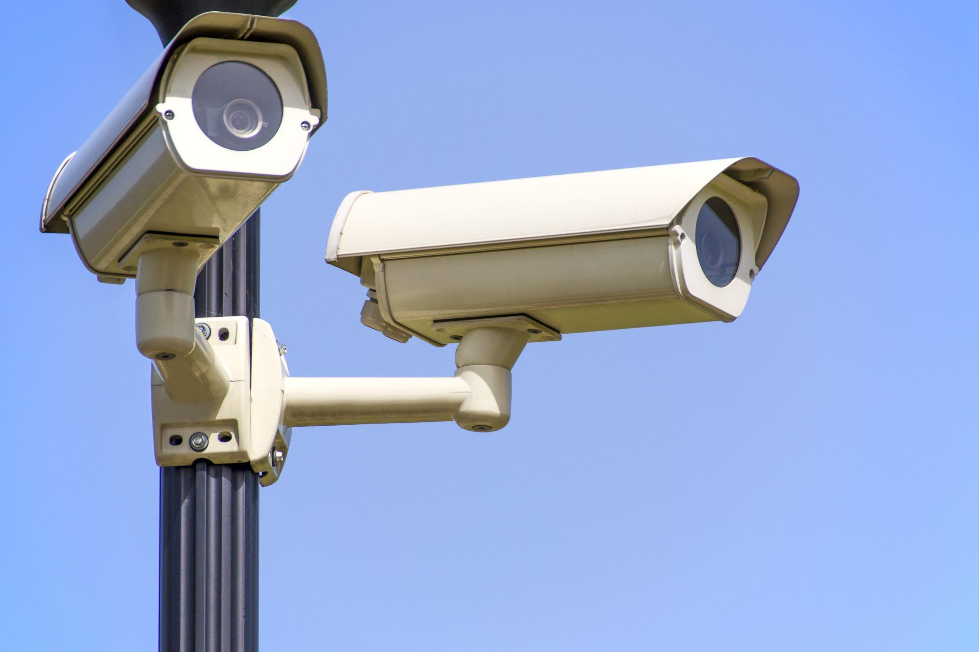 CCTV camera mounted on a black post under a clear blue sky.