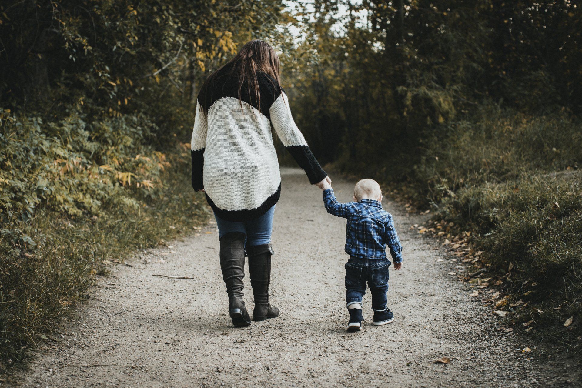 A woman and a child are walking down a dirt path holding hands.
