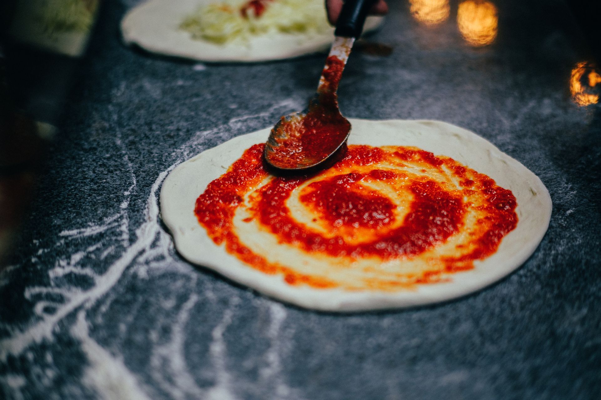 a person is spreading tomato sauce on a pizza with a spoon .