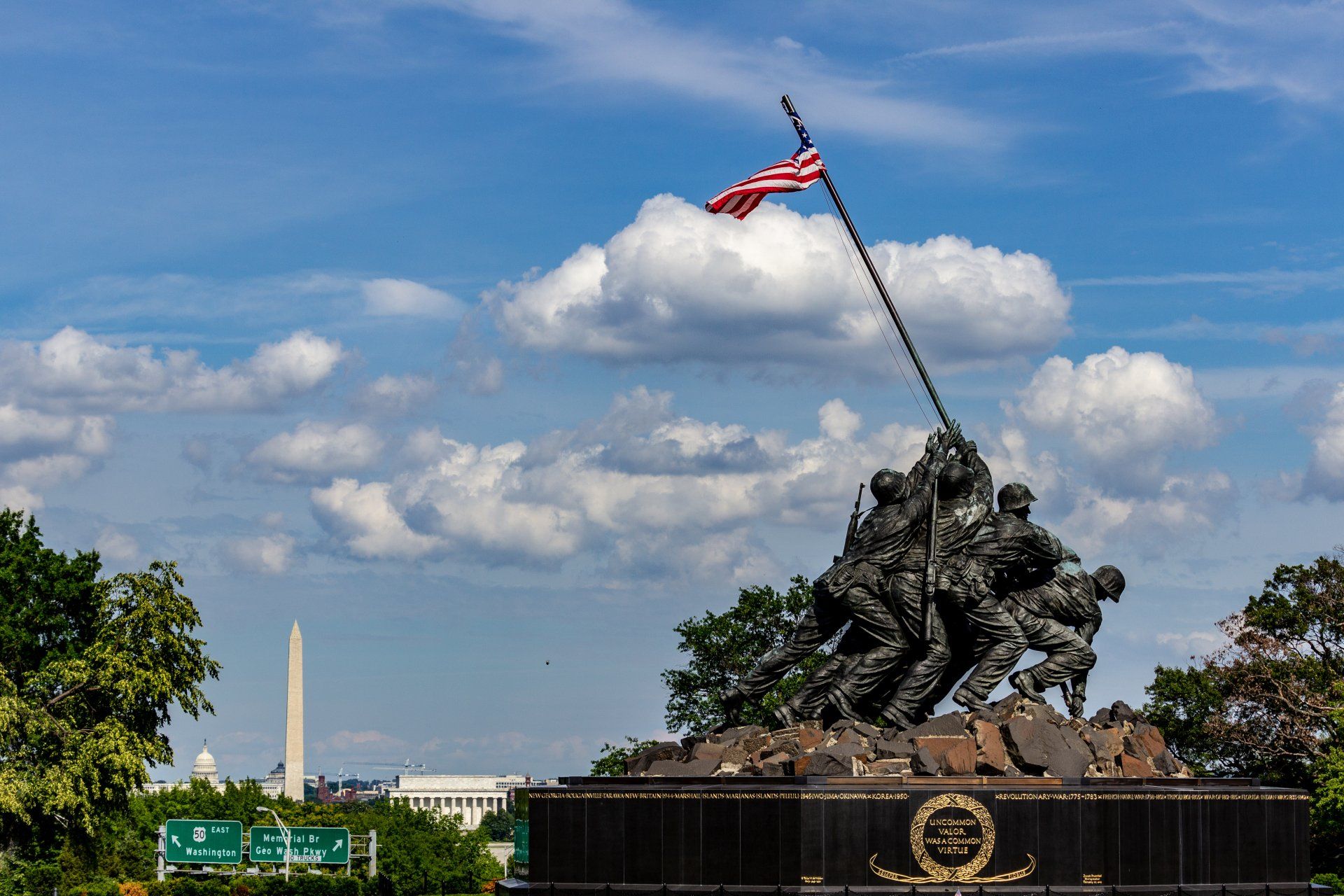 A statue of soldiers holding a flag in front of a cloudy sky.