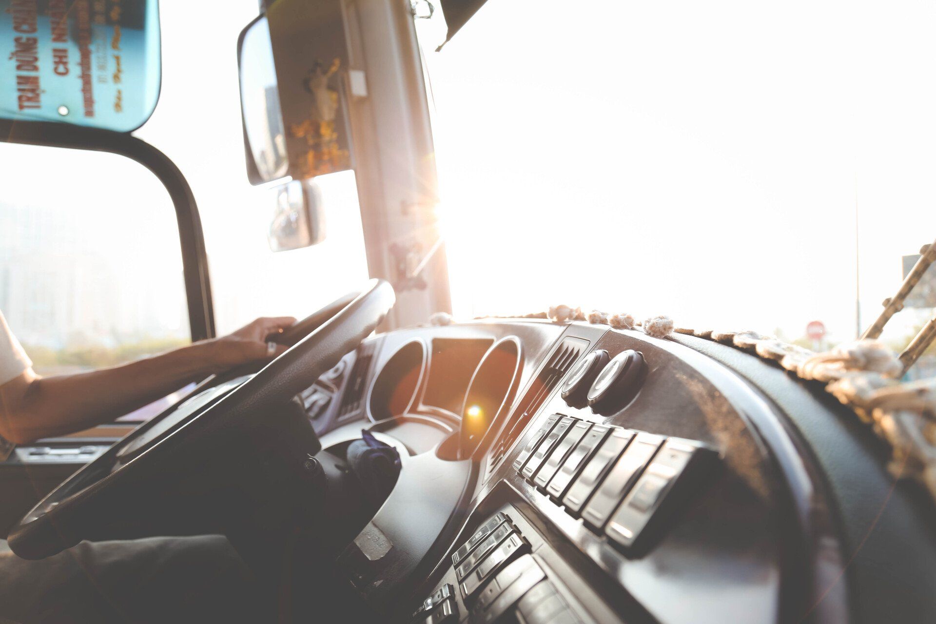 a man is driving a bus with the sun shining through the window .