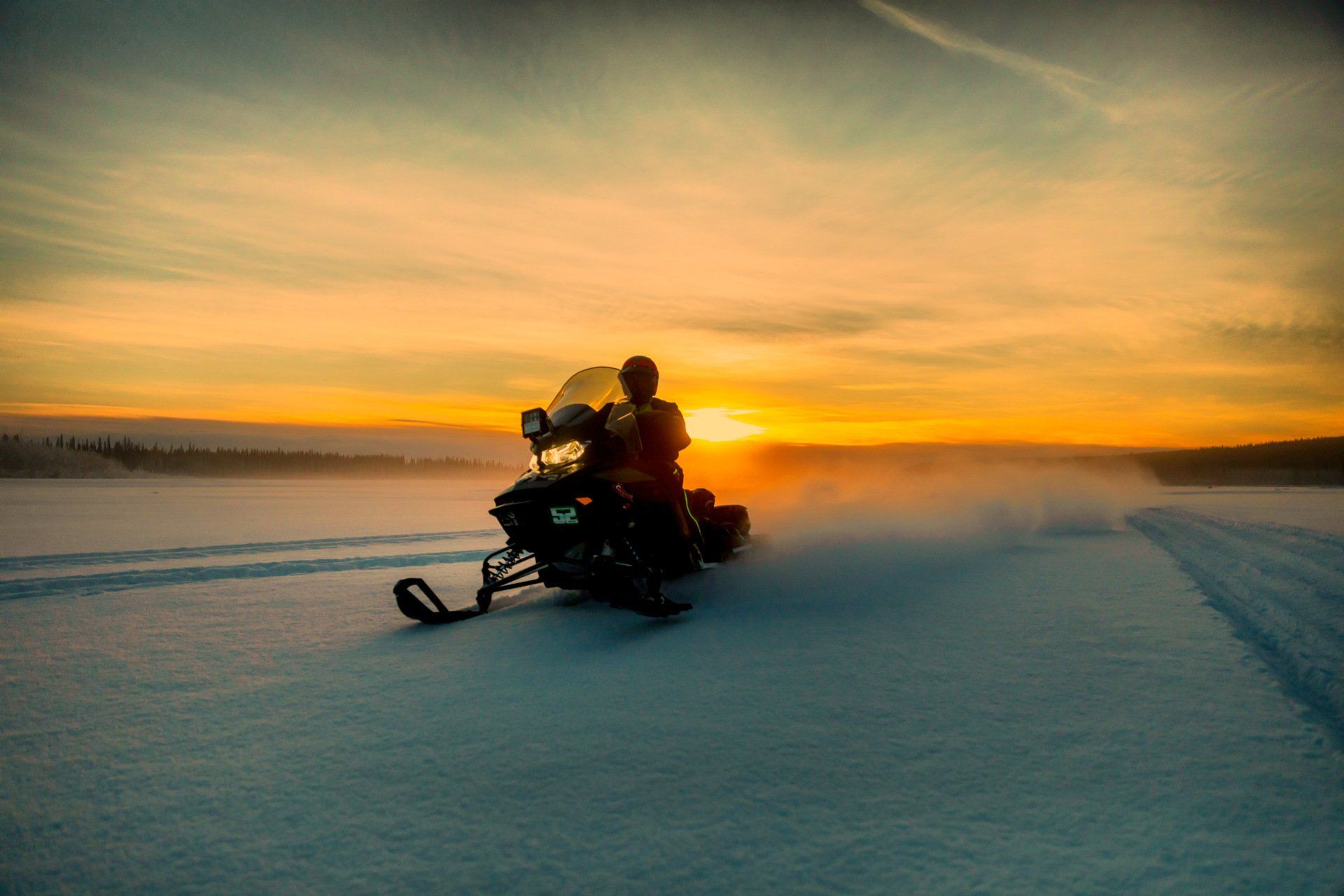 Person snowmobiling at sunset