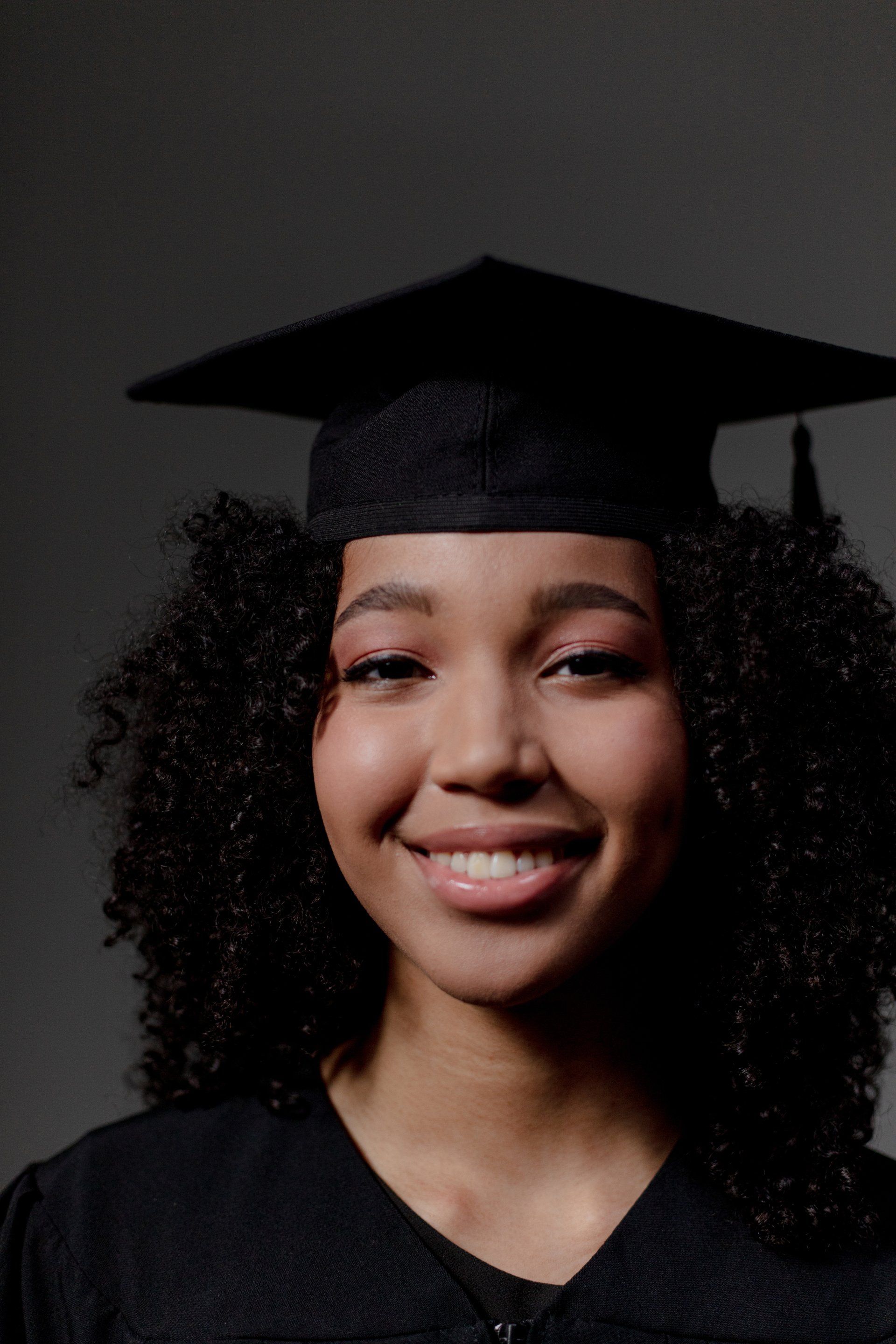 A woman wearing a graduation cap and gown is smiling.