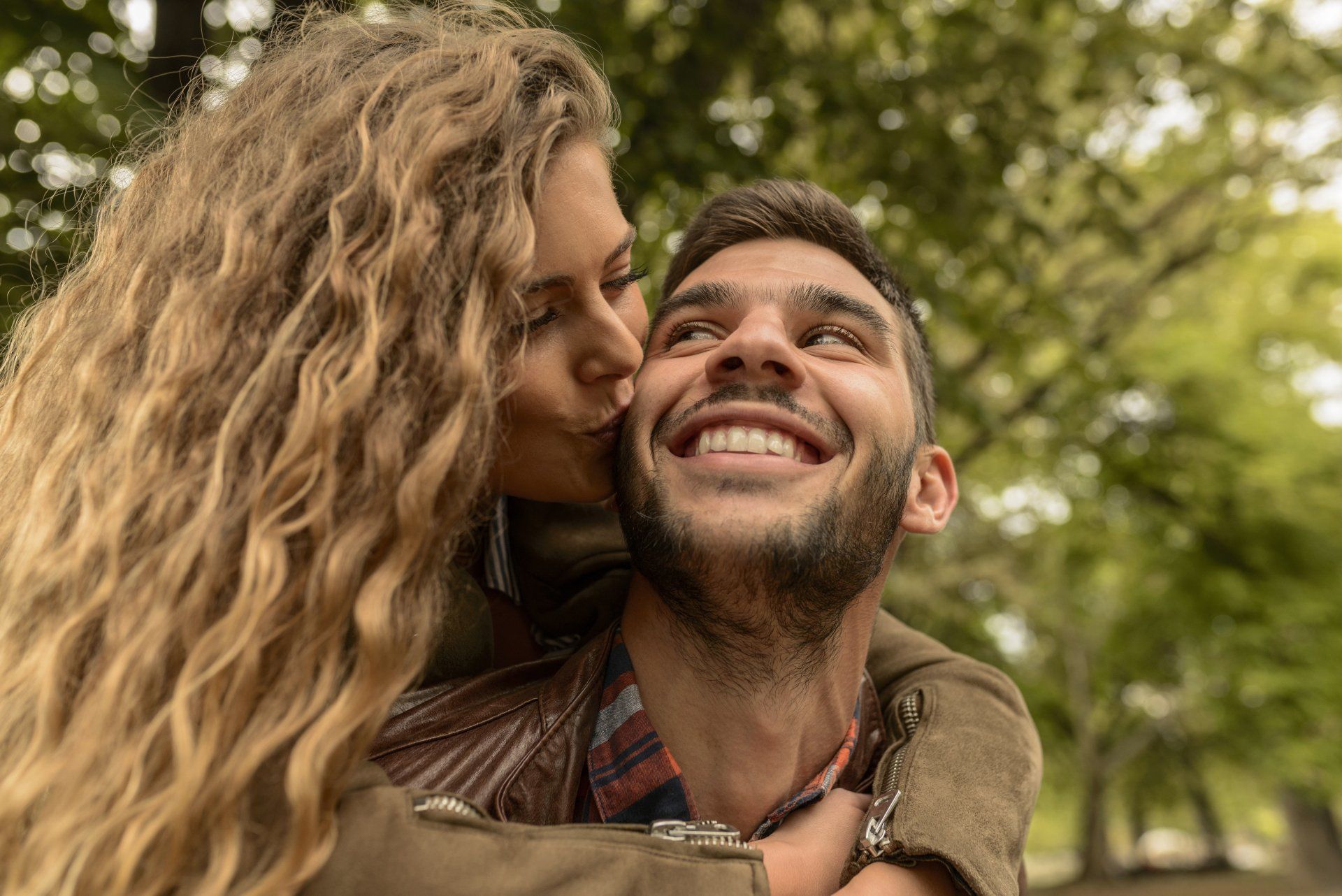 A woman is kissing a man on the cheek in a park.