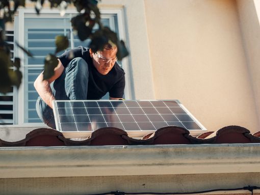 Ein Mann installiert ein Solarpanel auf dem Dach eines Hauses.