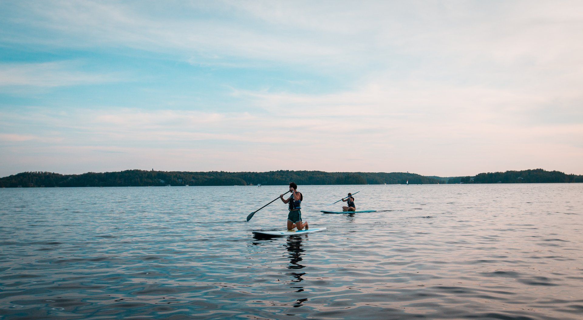 Two people are riding paddle boards on a lake.