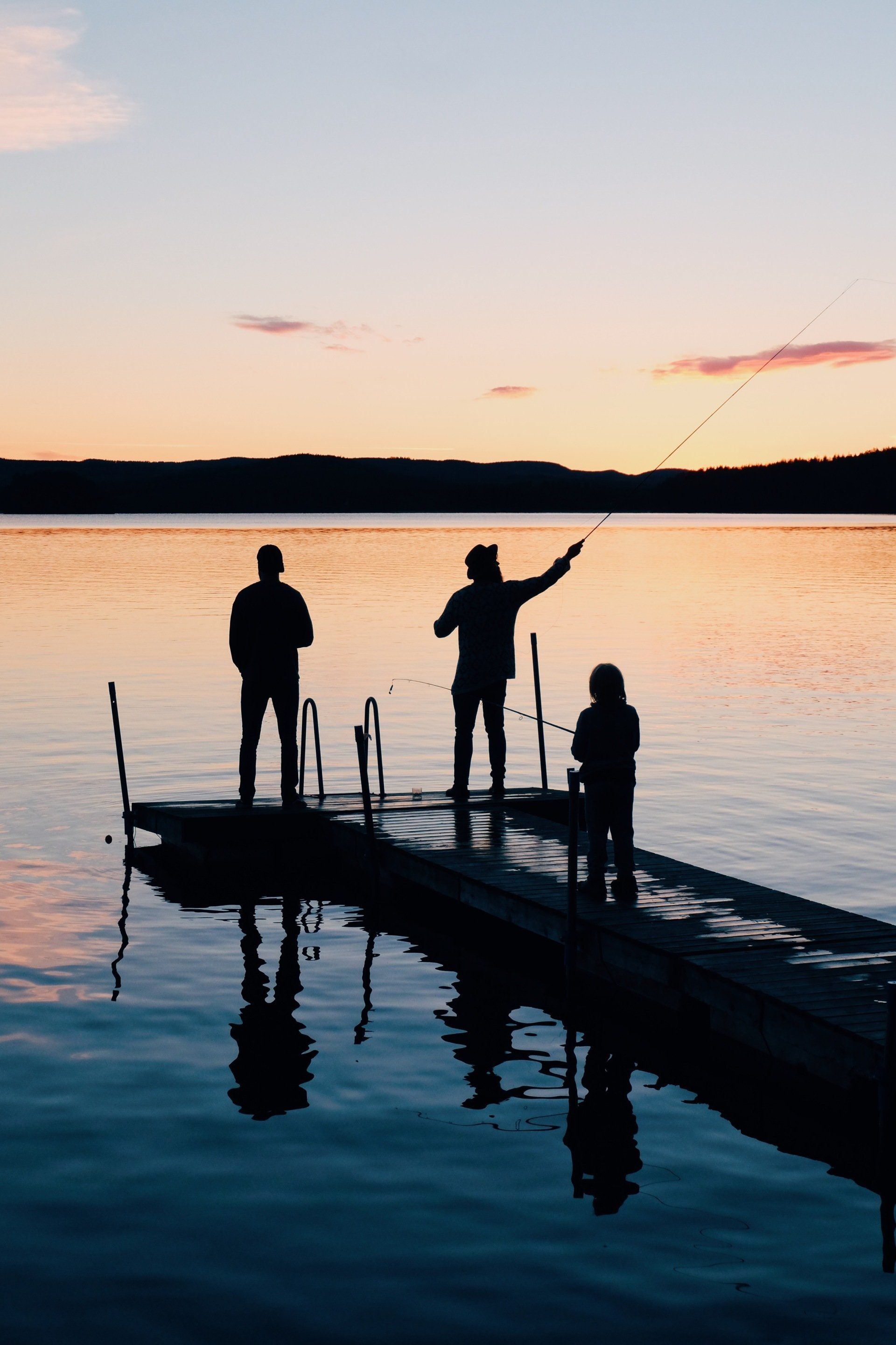 Three people are fishing on a dock at sunset