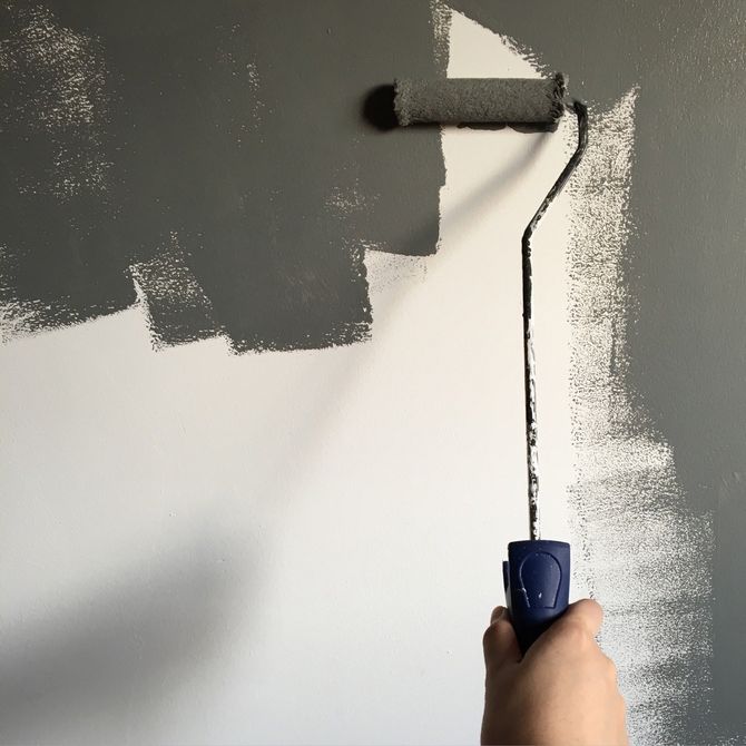 A person is using a paint roller to paint a wall