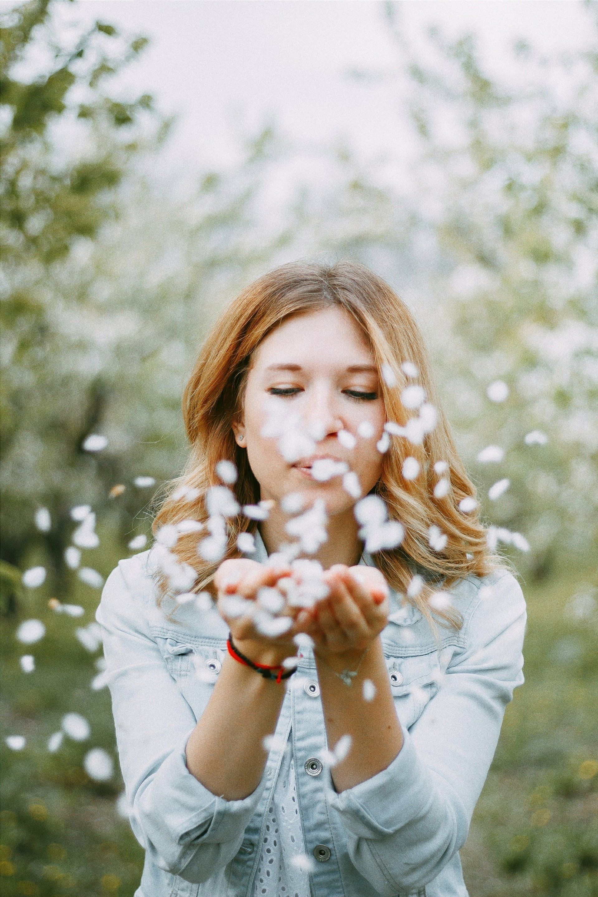 A woman is blowing petals out of her hands in a park.