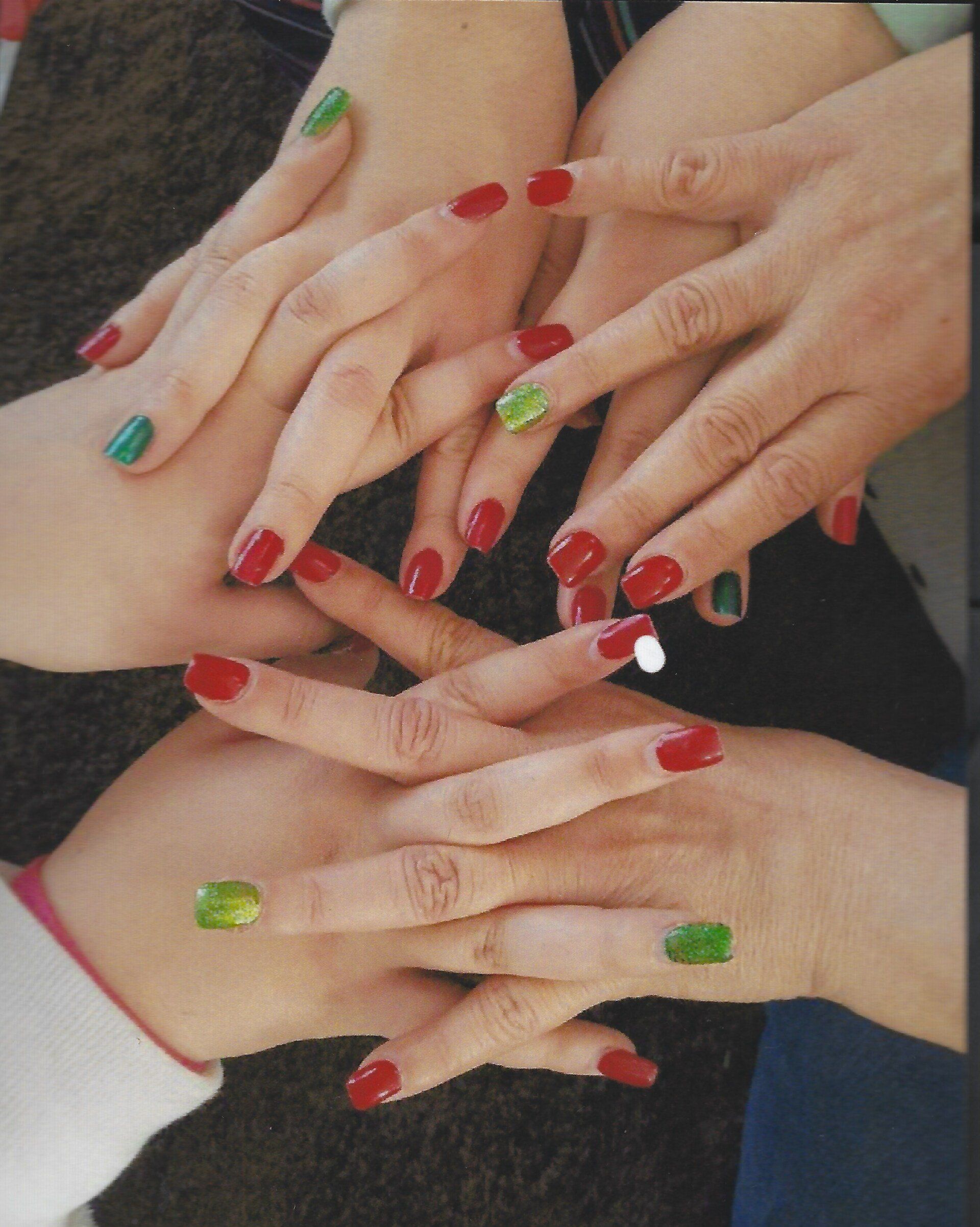 A group of hands with red and green nails are stacked on top of each other