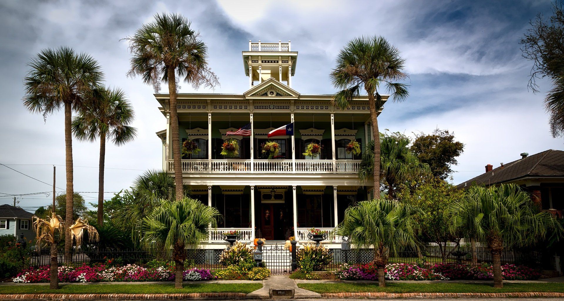 Historic white mansion with flags, palm trees, and lush garden in Galveston.