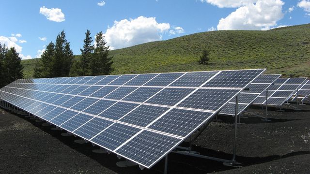 Solar panels on hillside with trees and mountains, capturing solar energy.