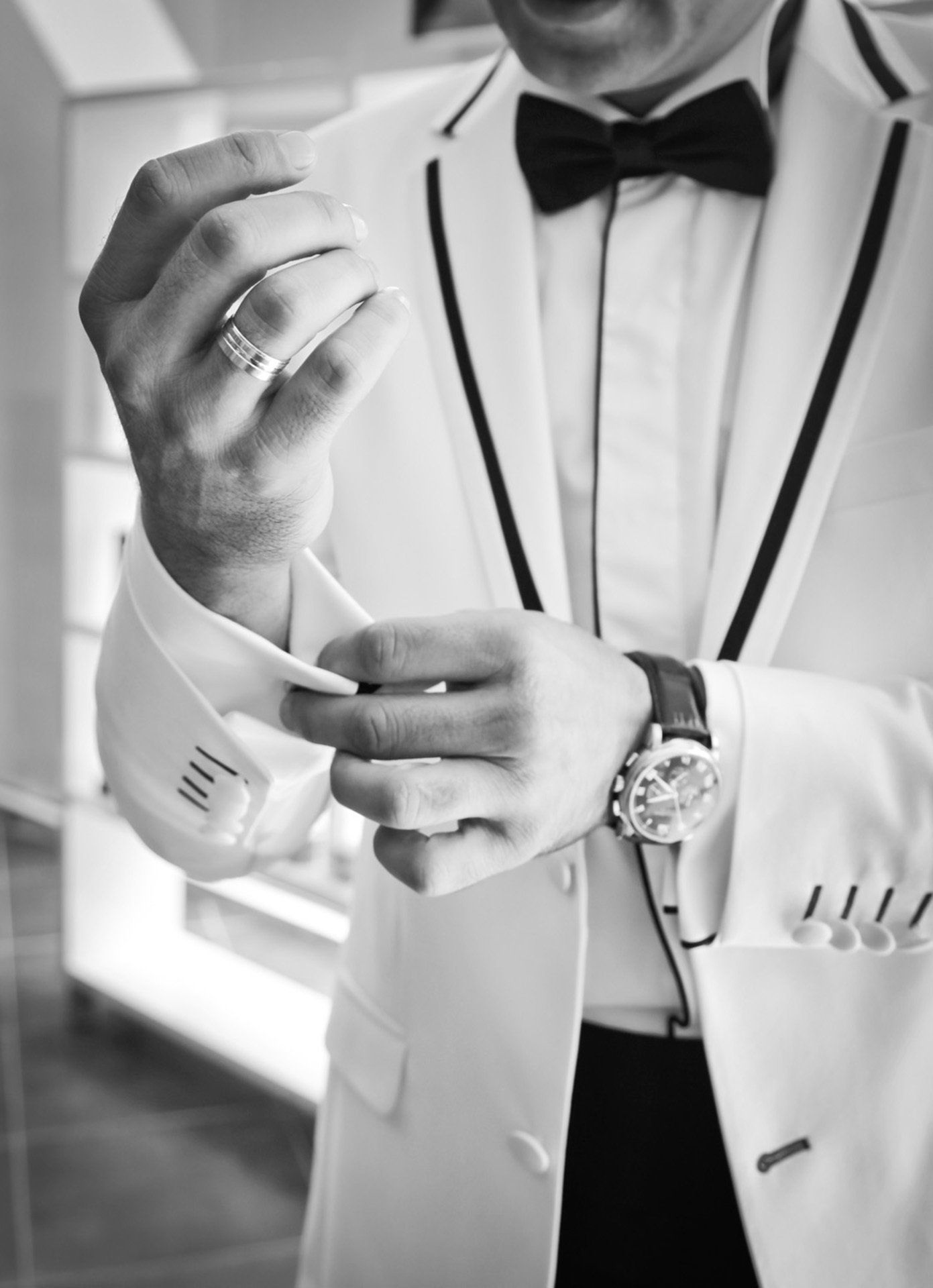 A man in a tuxedo and bow tie is adjusting his cufflinks