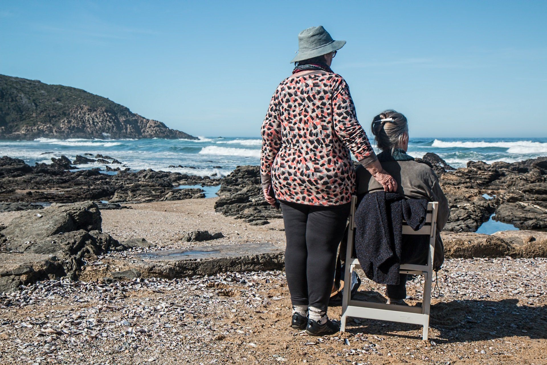 A woman is standing next to a woman in a wheelchair on the beach.