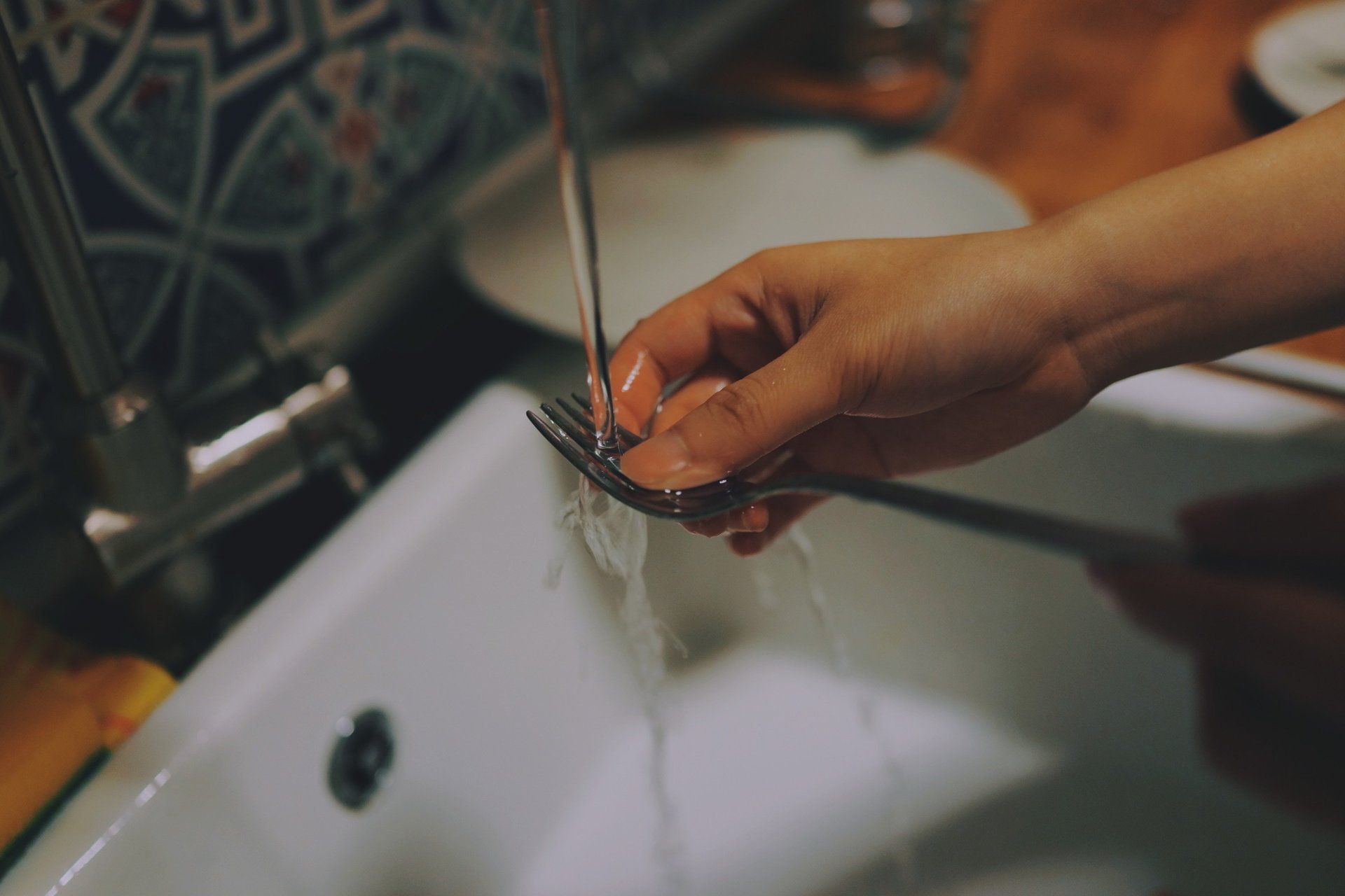 A person is washing a fork in a sink.