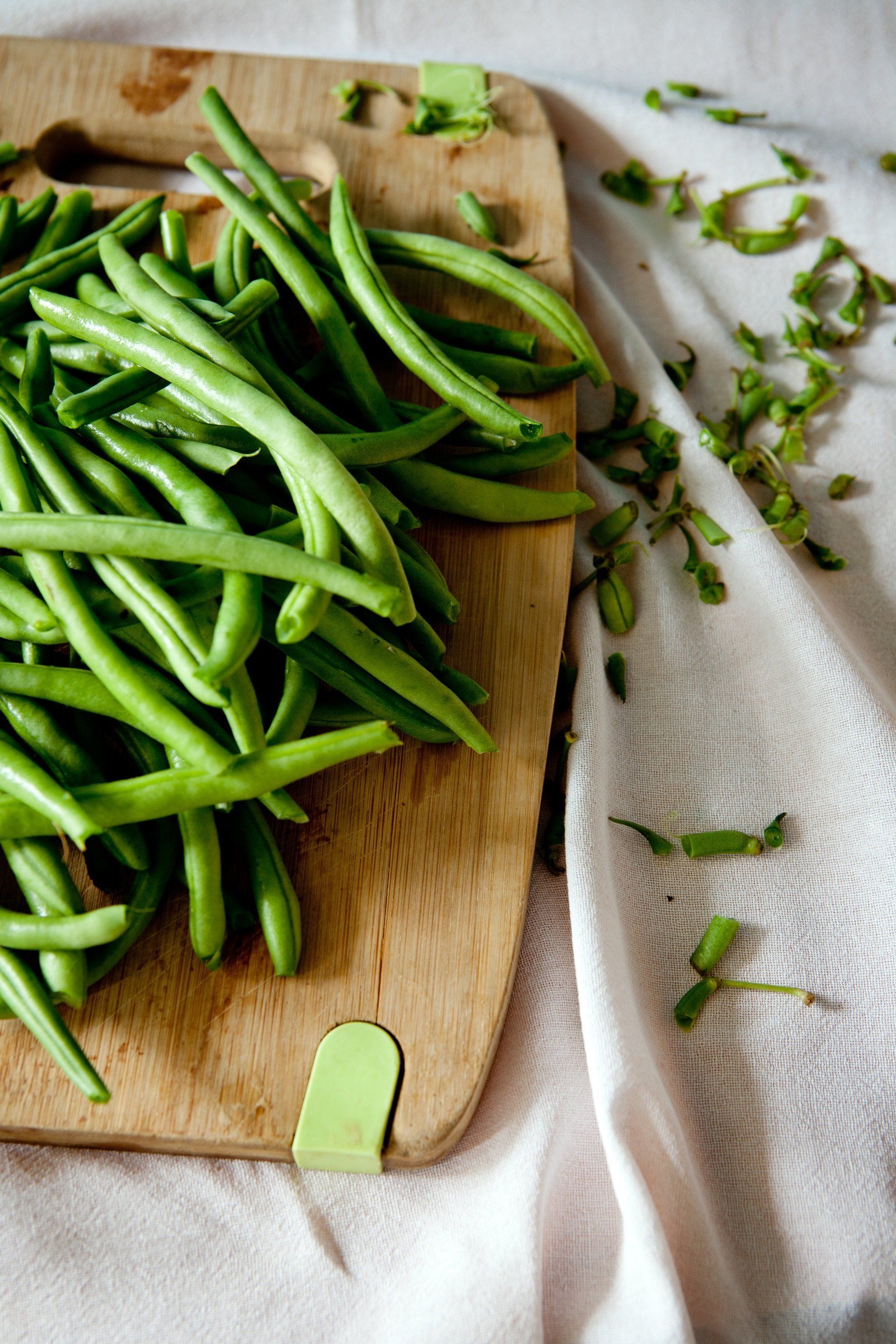 Green beans are sitting on a wooden cutting board.