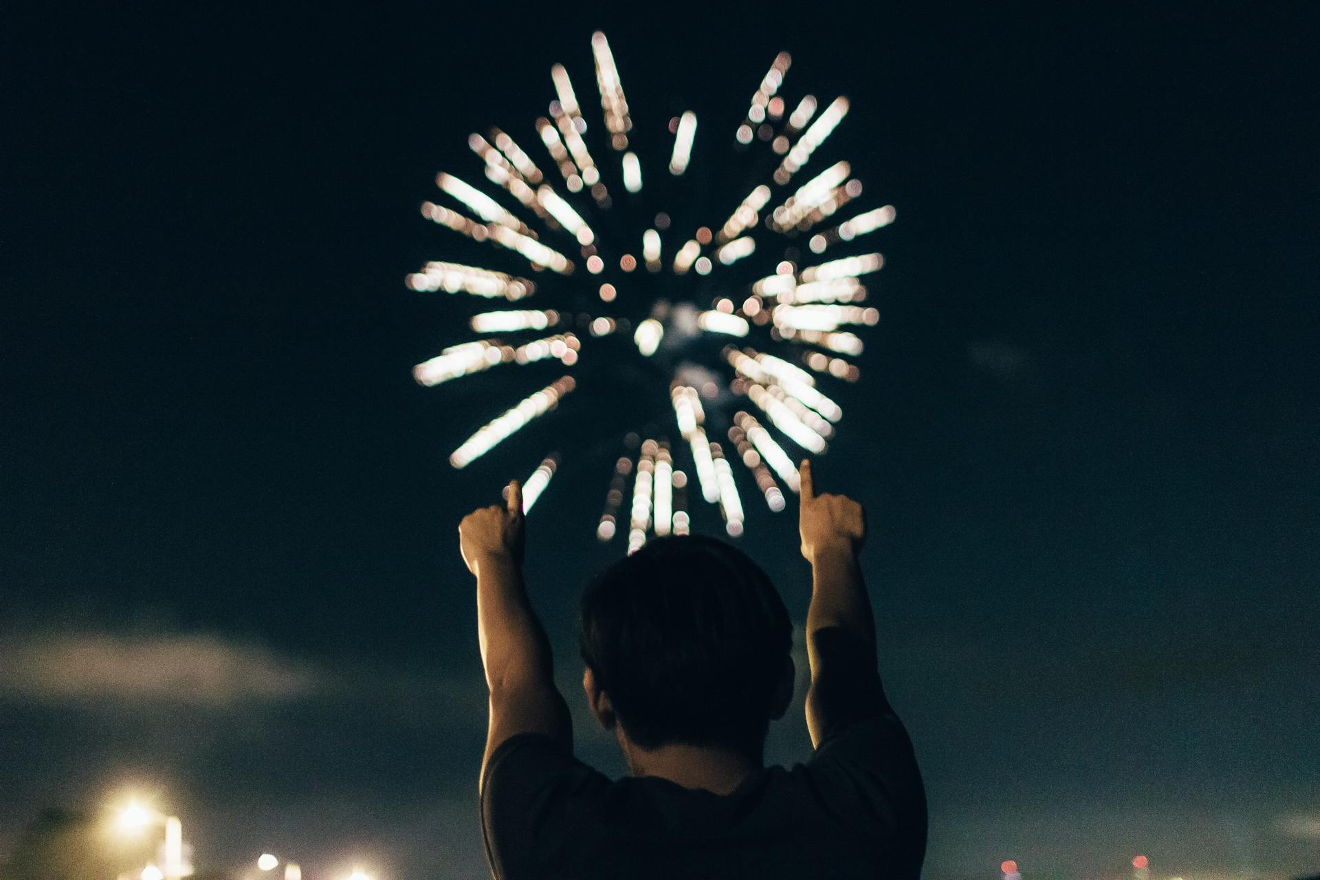 man reaching up to the skyies with fireworks in the distance