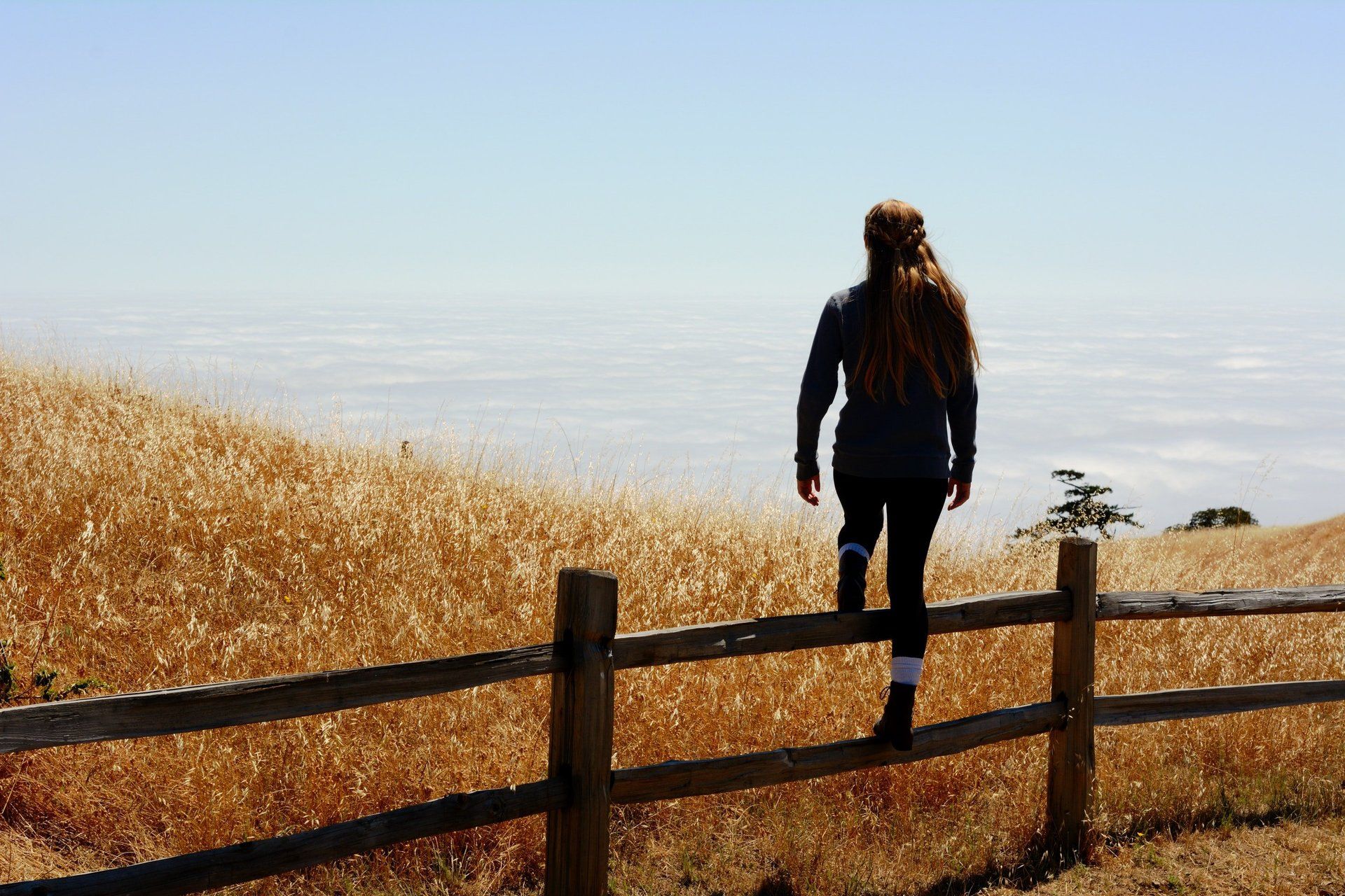 A woman is walking across a wooden fence in a field.
