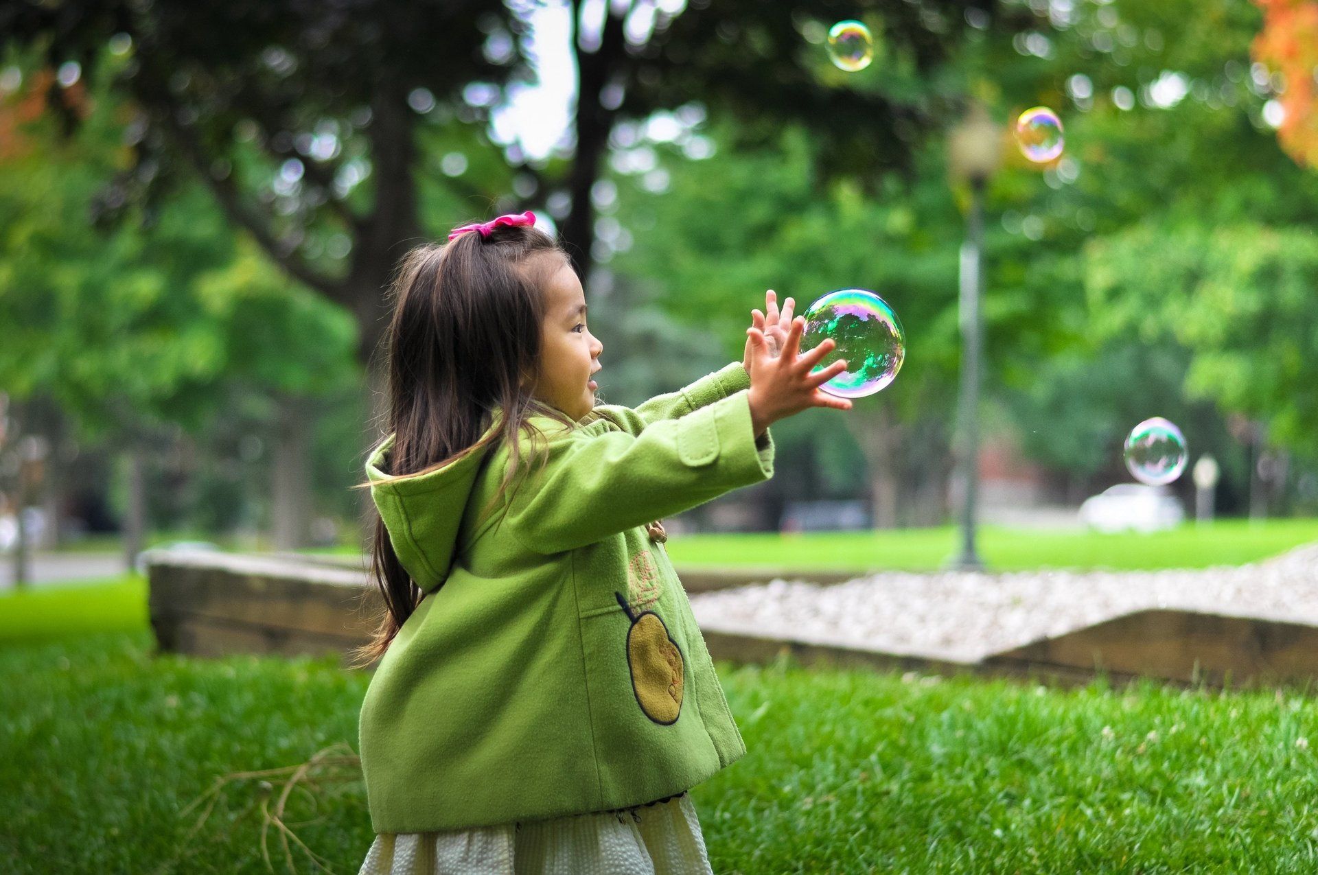 A little girl is playing with soap bubbles in a park.