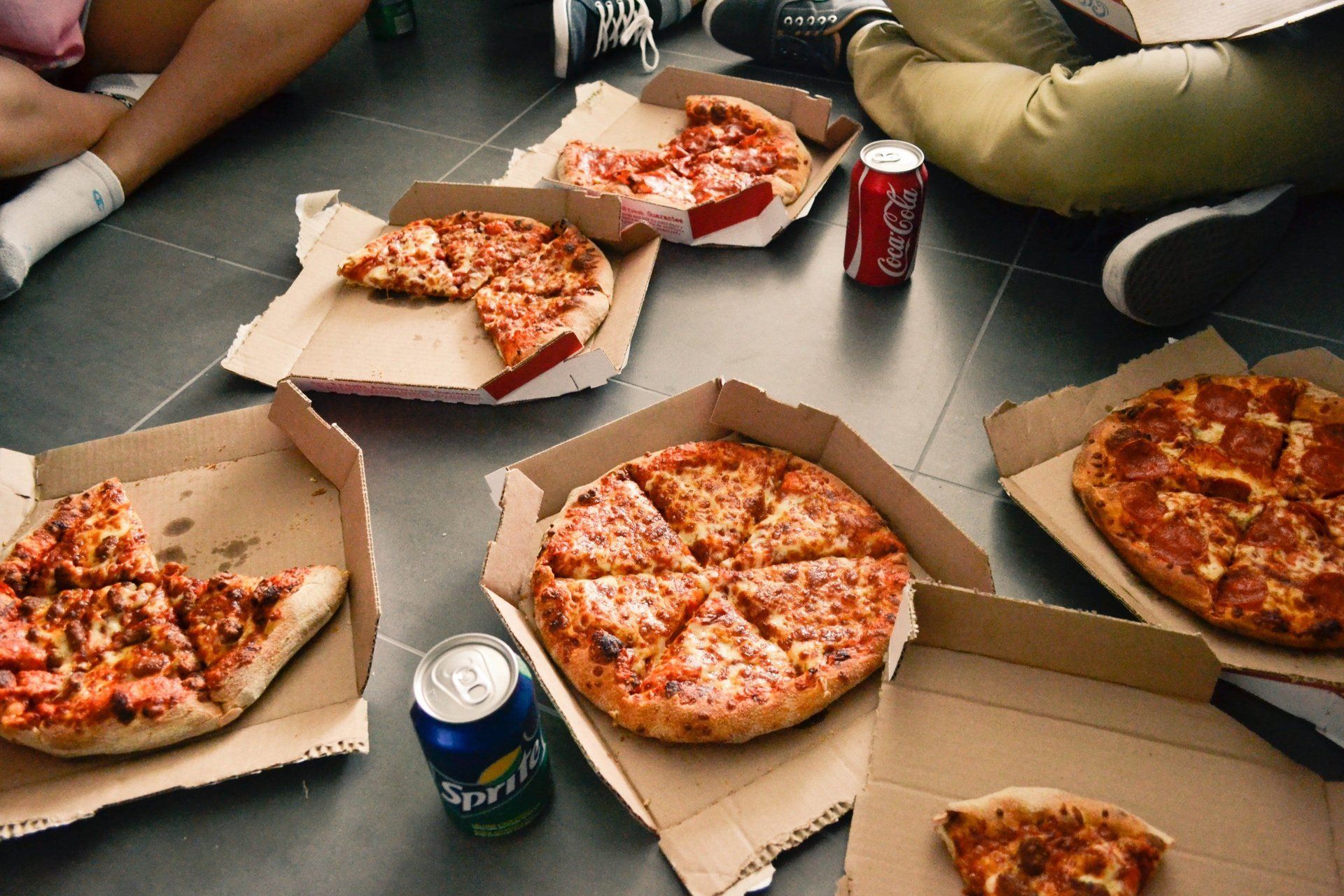a group of people are sitting on the floor eating pizza and drinking soda .