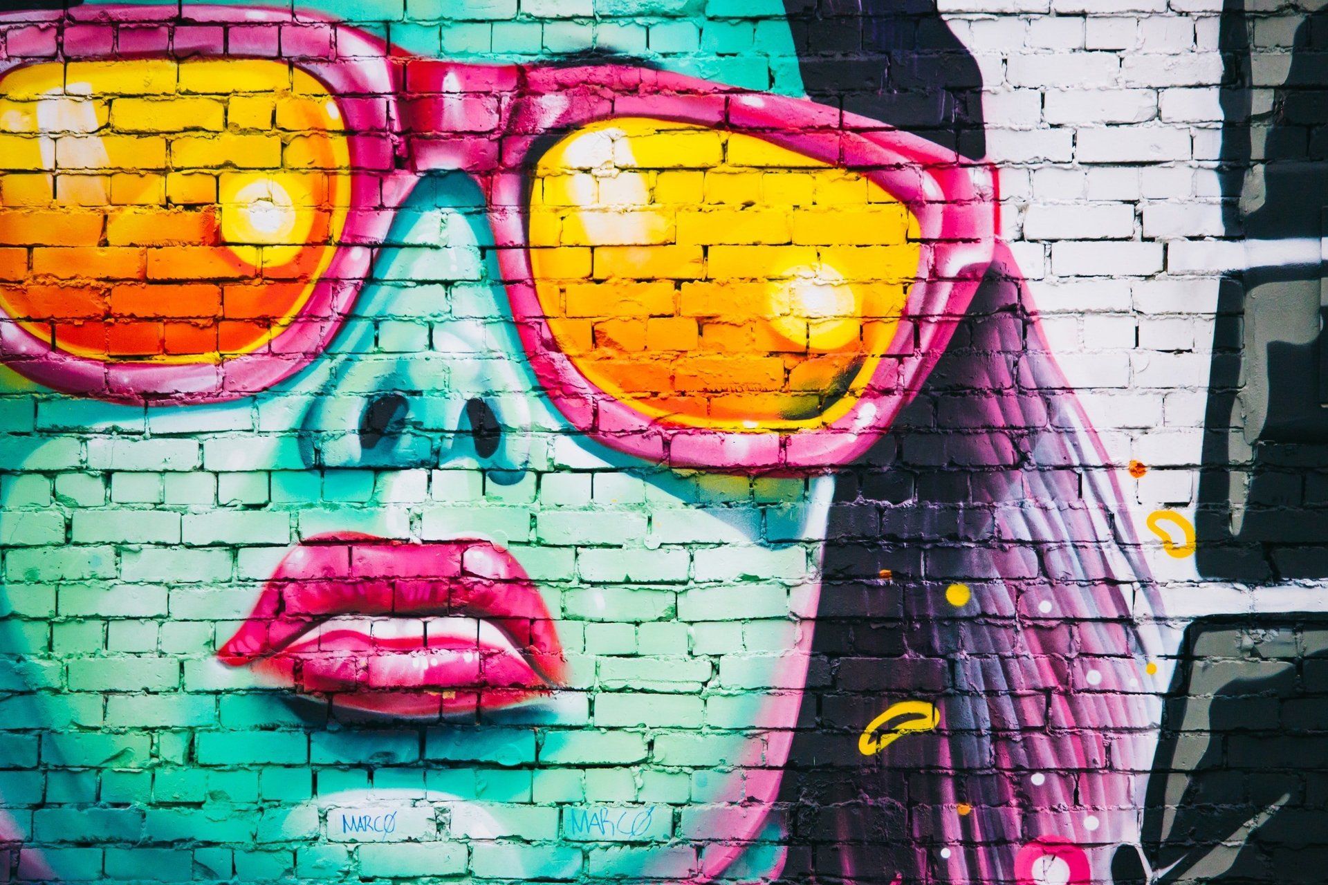 Un dipinto graffiti di una donna che indossa occhiali da sole su un muro di mattoni.
