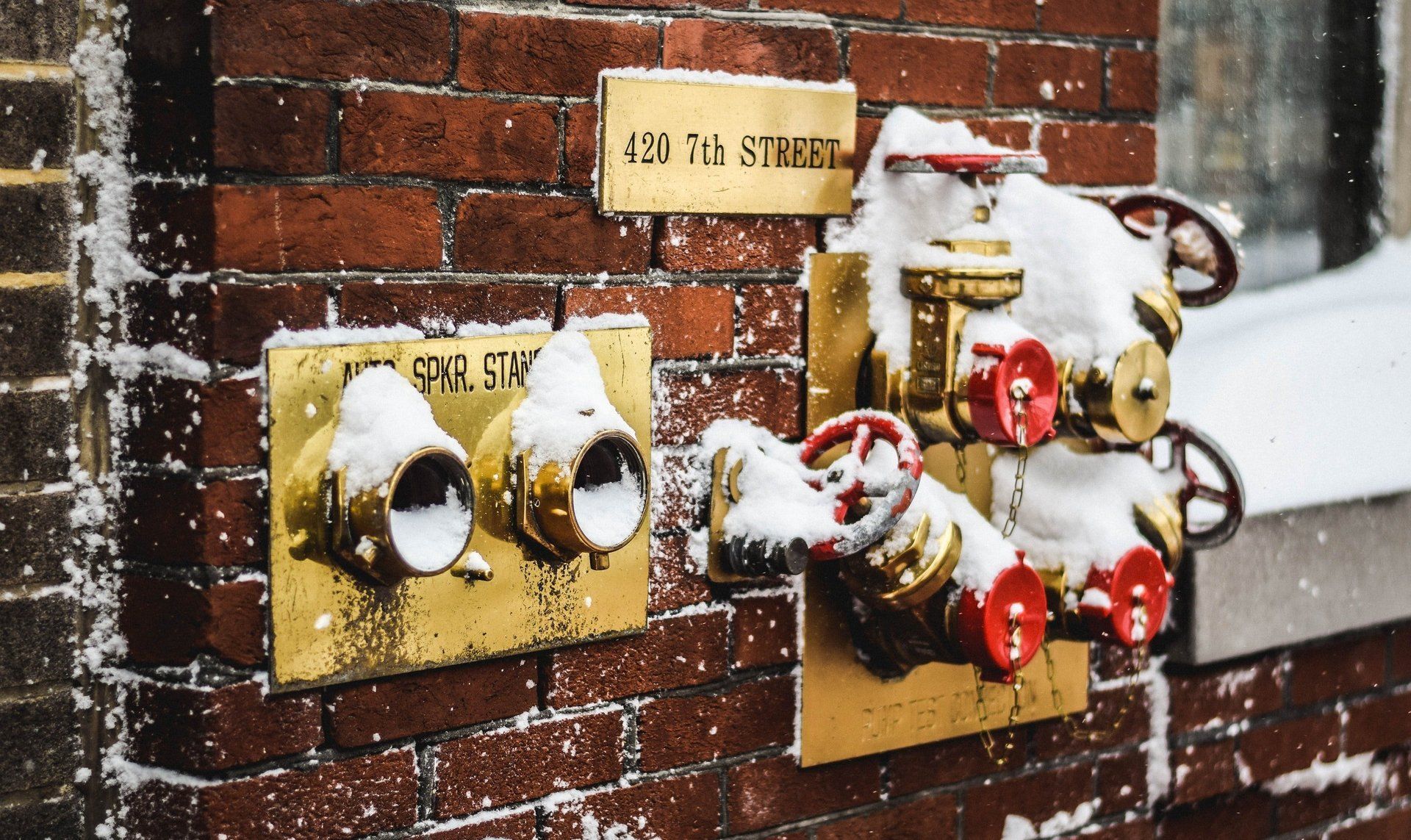 Two fire hydrants are covered in snow on a brick wall.
